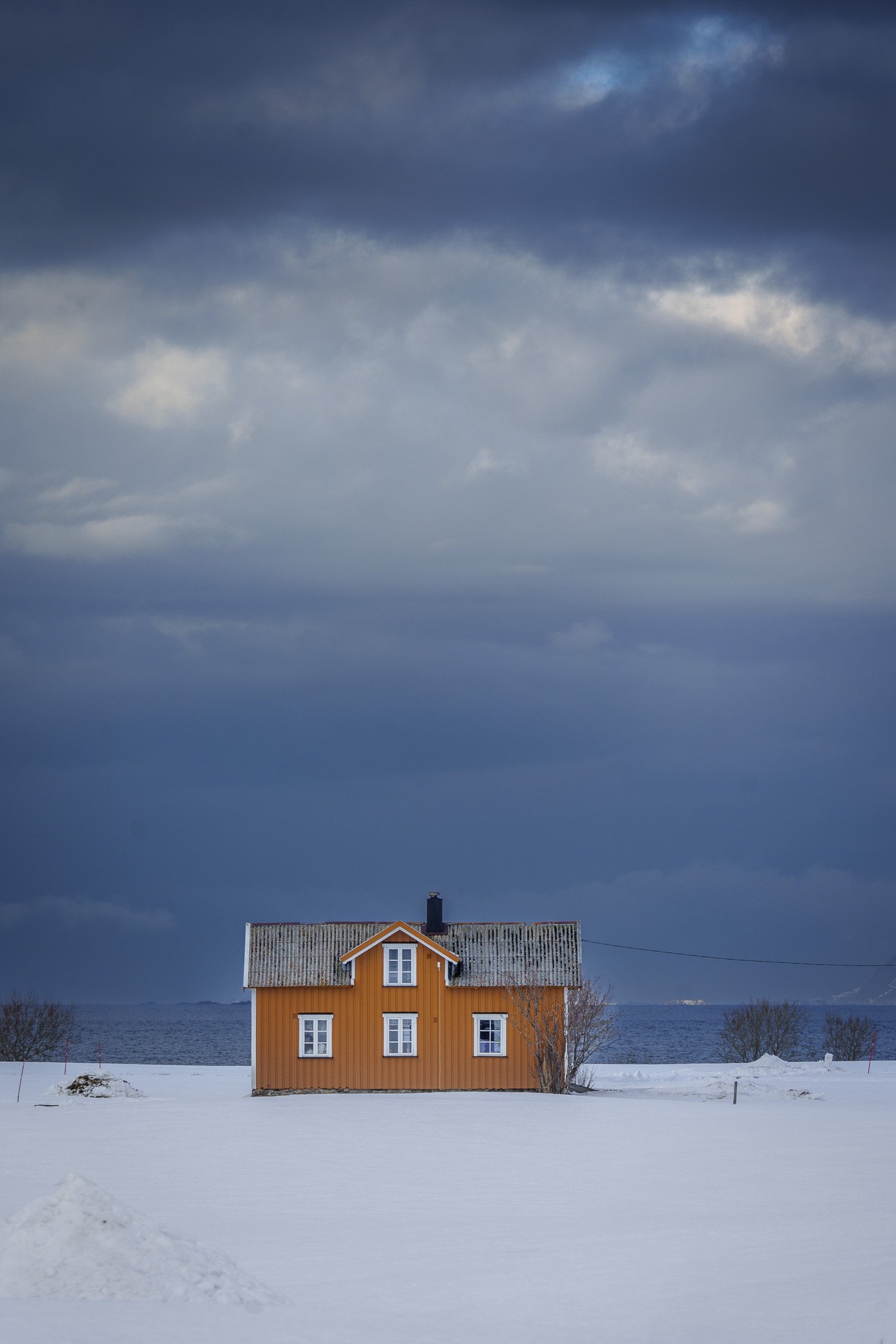 Orange traditional house on snow-covered coast under dramatic clouds, Lofoten Islands, Norway
