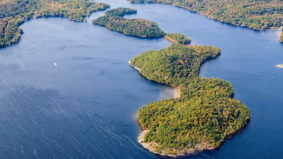 Aerial view Lake of Bays, ON with a winding, tree-covered peninsula extending into a large body of water, surrounded by forested land.