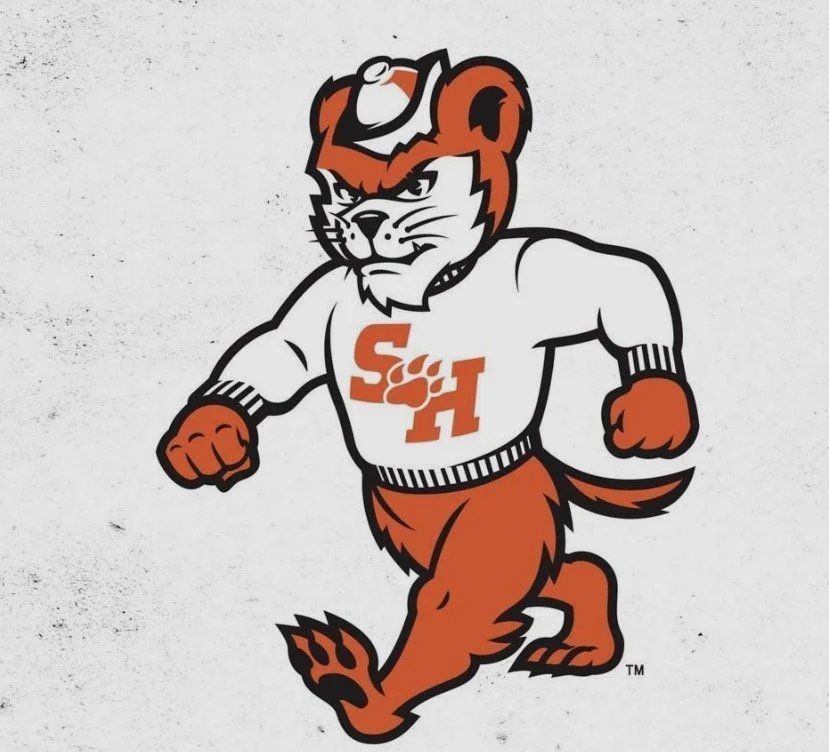 Cartoon mascot of a lion in a running pose, wearing a white hockey jersey with orange lettering 'S H' and a paw print, and an orange lion's tail and fur.