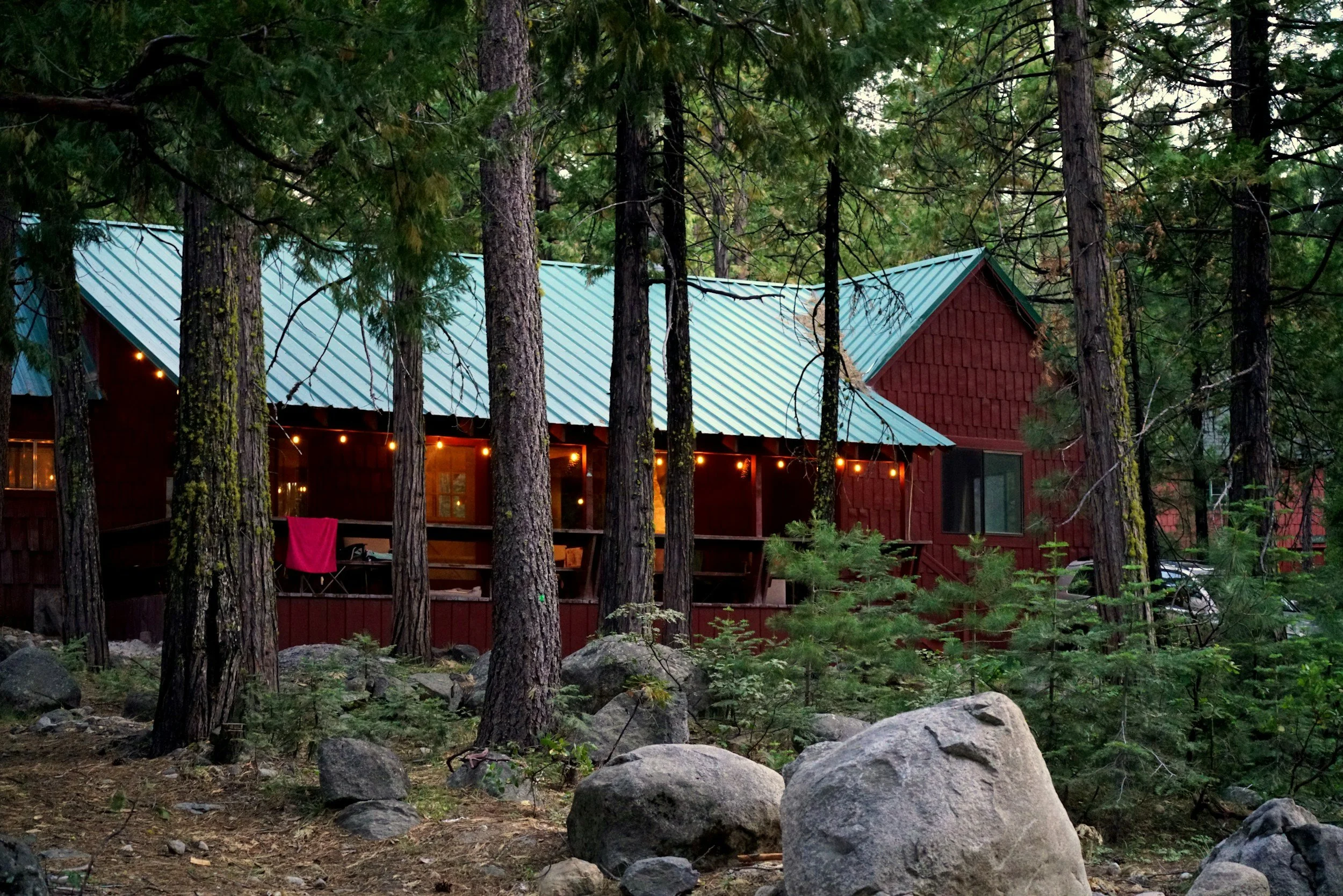 A stock image of a red cabin in the middle of the forest with fairy lights hung over the balcony.