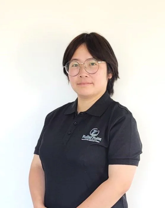 A woman with short black hair and glasses wearing a black polo shirt with a logo that says 'Ruler Point' against a plain white wall.