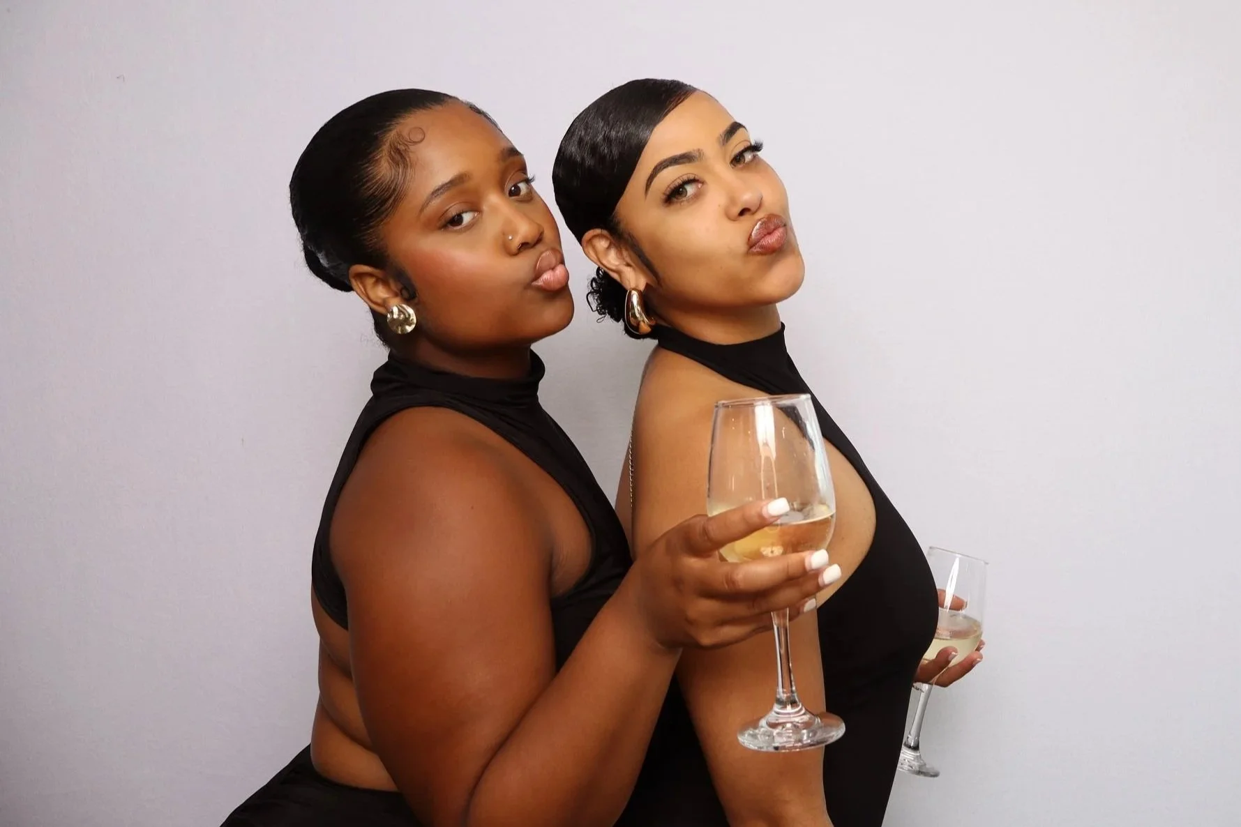 Two guests posing with drinks for a studio-style event portrait, with a white backdrop, in Bermuda