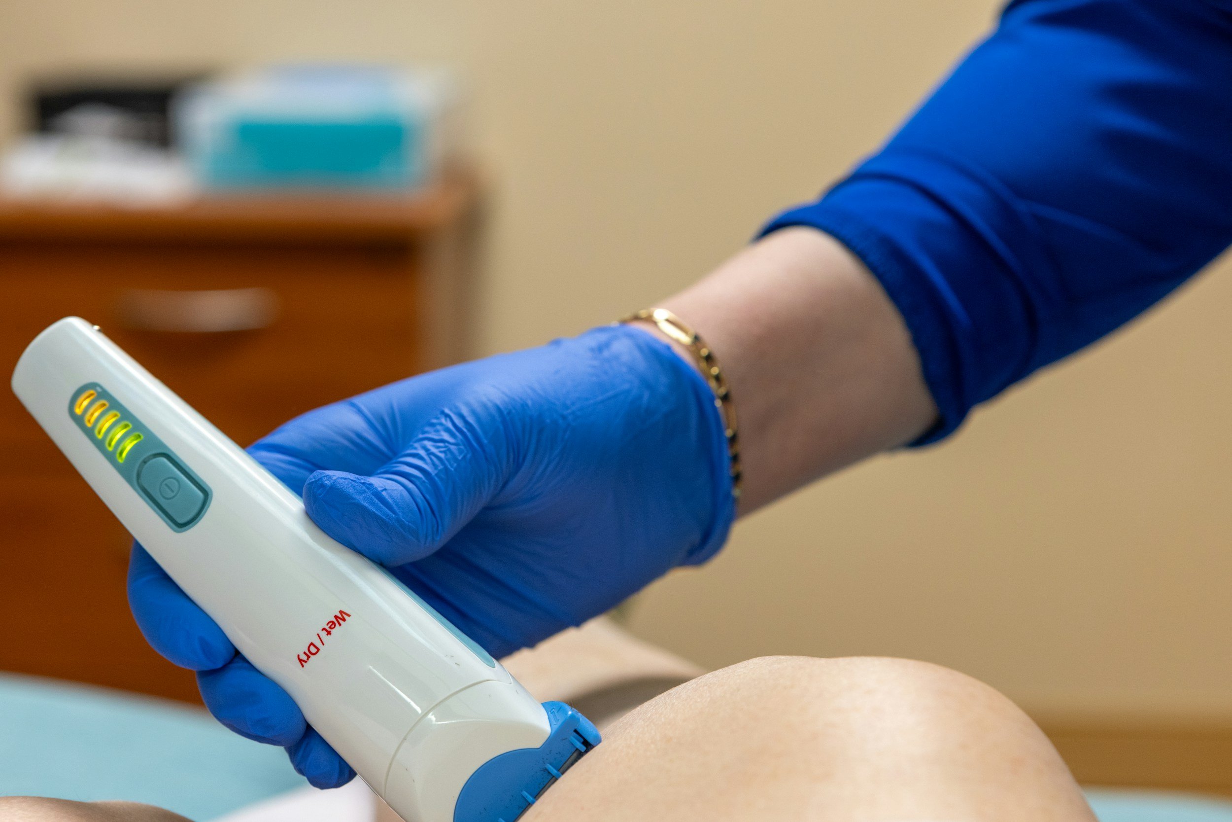 A medical professional wearing blue gloves is using a handheld ultrasound device on a patient's leg.