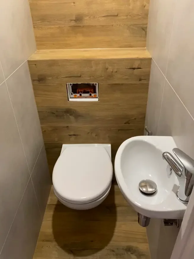 Łazienka z podtynkową spłuczką Geberit, wiszącą toaletą, umywalką oraz płytkami drewnopodobnymi.