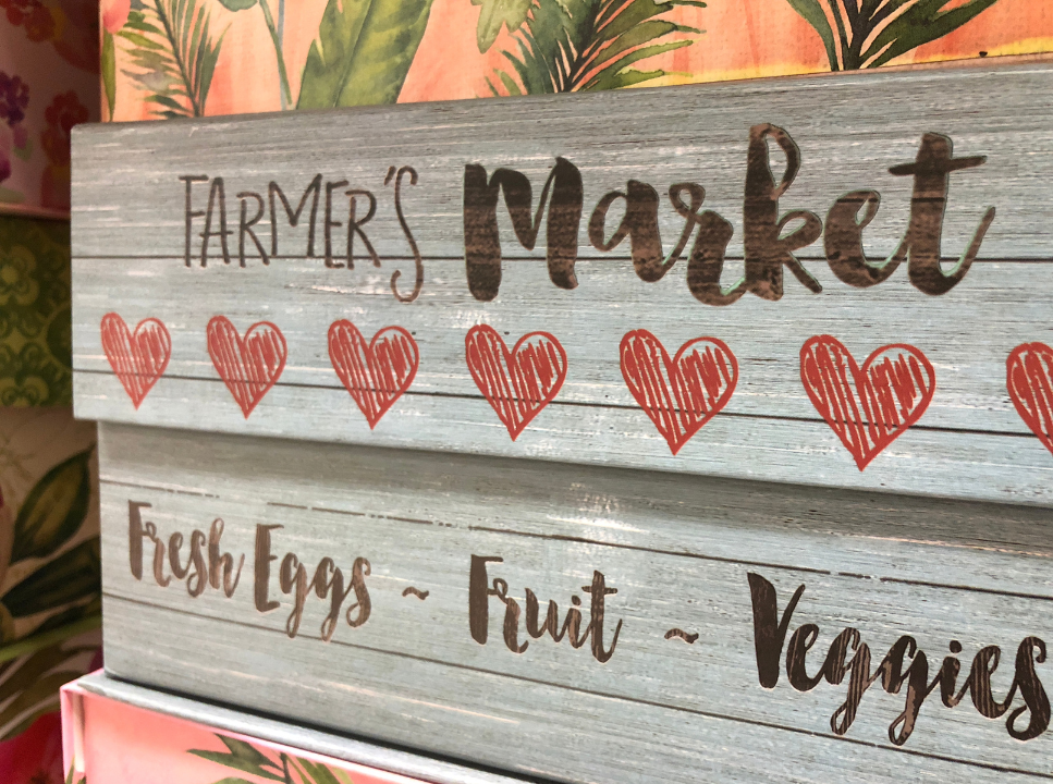 A wooden sign with the words "Farmer's Market" and red hand-drawn hearts below it. The sign also lists "Fresh Eggs," "Fruit," and "Veggies".
