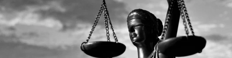 Close-up of a statue of Lady Justice holding scales against a cloudy sky.