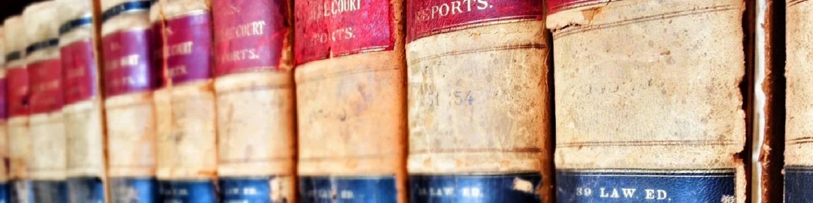 A row of old, worn legal books with red, white, and blue spines on a bookshelf.