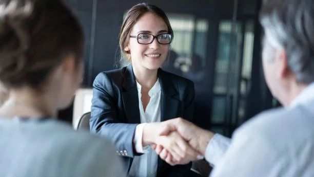 A woman in a business suit shaking hands with two other people in a professional setting.