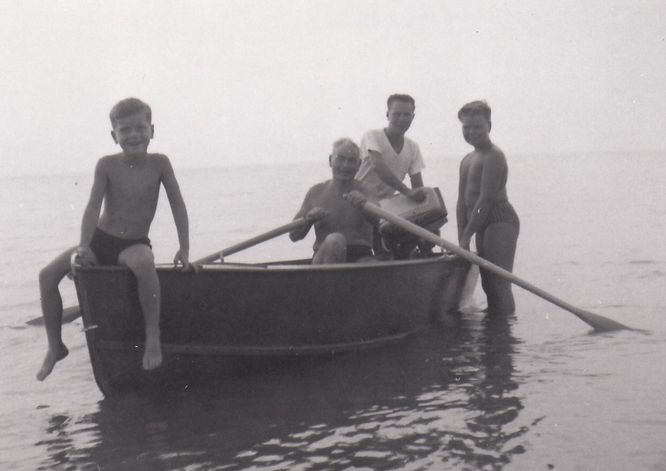 Four children and an elderly woman on a small boat in shallow water at the beach, smiling and enjoying a day out.