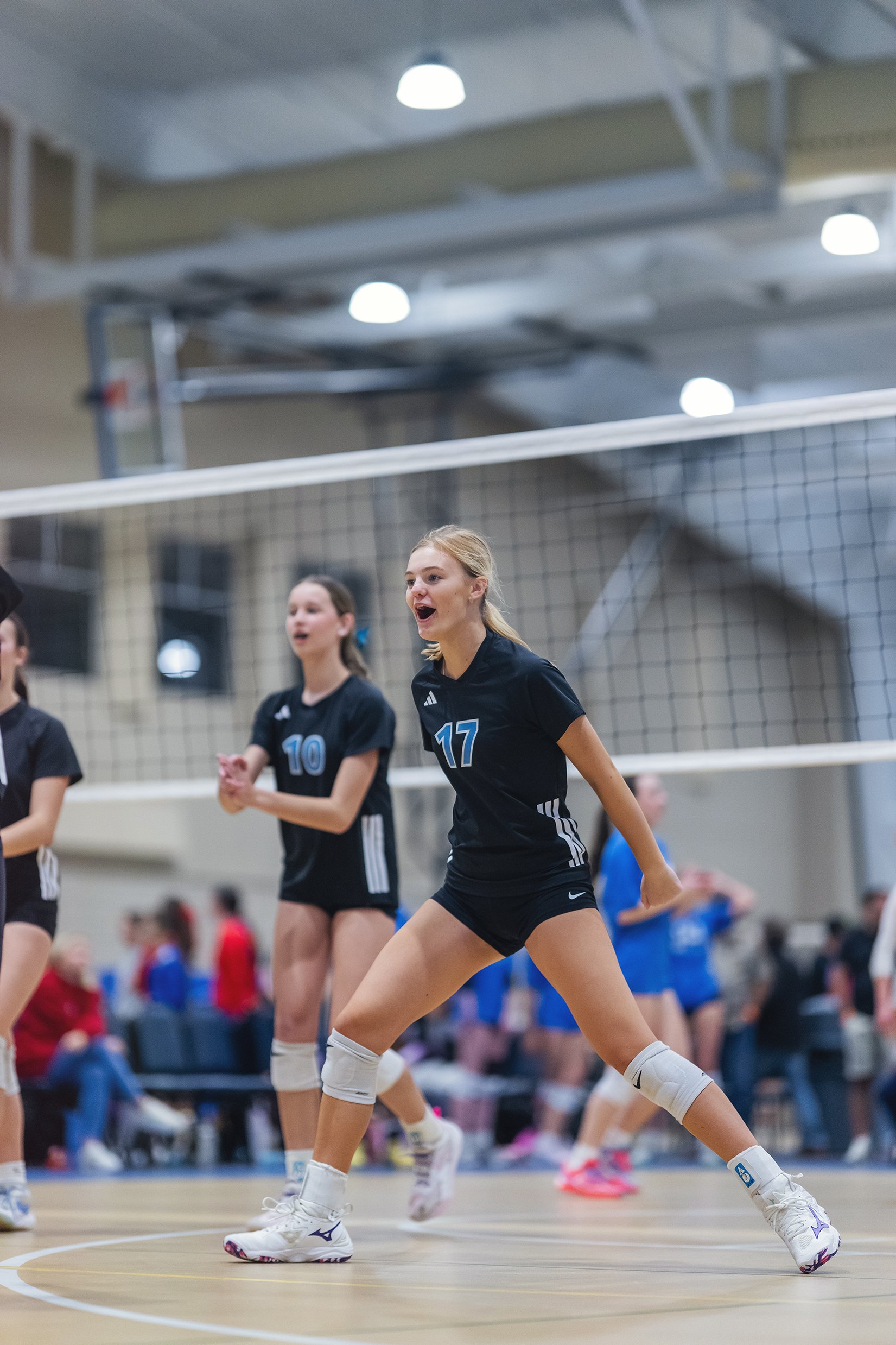 A group of female volleyball players are on an indoor court, wearing black uniforms with numbers, actively engaged in a game.