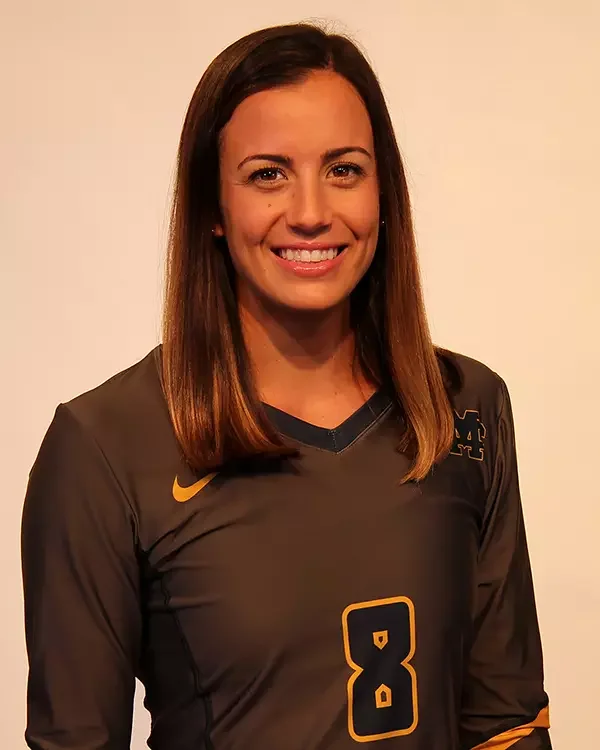 Smiling woman with straight brown hair wearing a black sports jersey with the number 8 and a Nike logo, standing against a plain background.