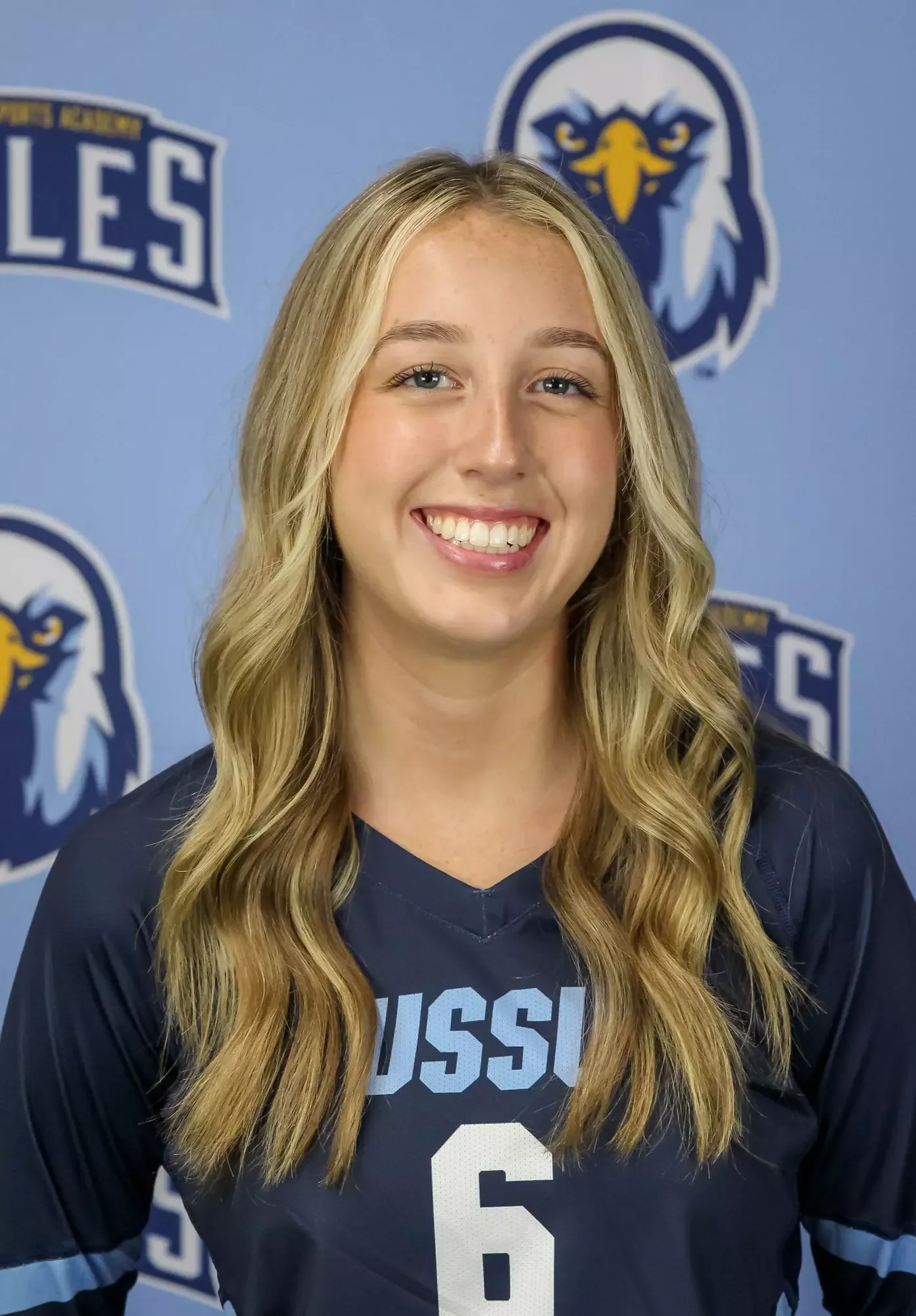 Young woman with long blonde hair smiling in front of a Detroit Lions logo and a sports team jersey.