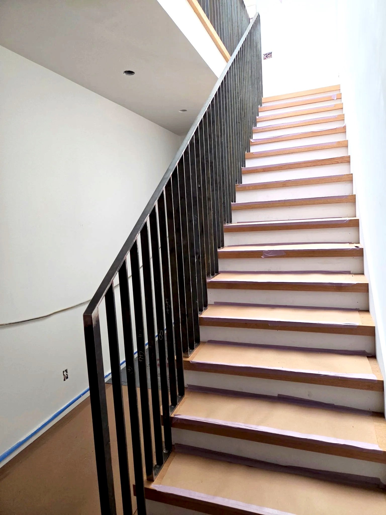 Begadon Welding & Fabrication working at an interior of a stairway under construction with wooden steps and black metal railing, white walls, and welding railings
