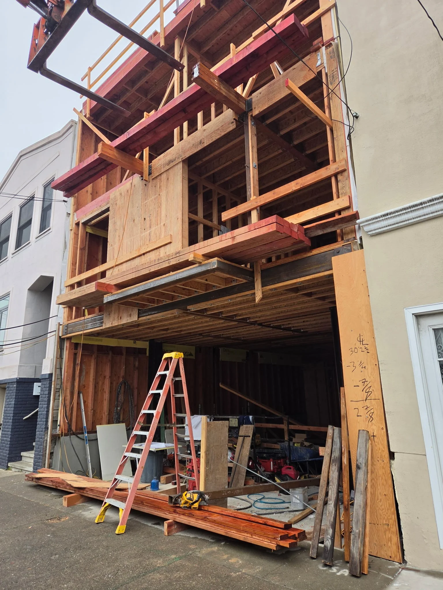 Begadon Welding & Fabrication working at a Construction site of a building with framed wooden structure, scaffolding, stairs, and construction tools and materials on the sidewalk.
