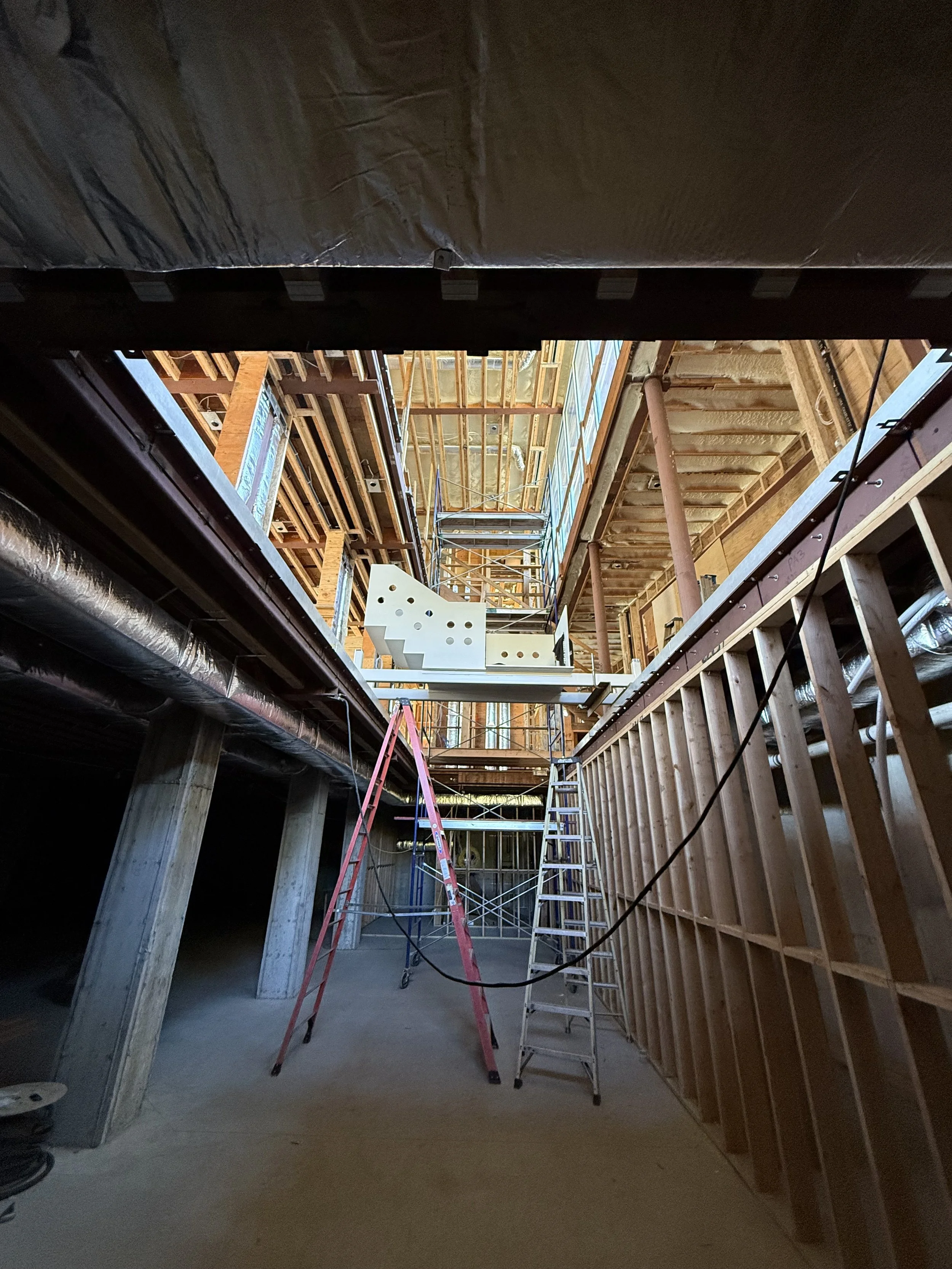 Construction site with unfinished wooden framing and scaffolding inside a building under construction, with ladders and pipes visible.
