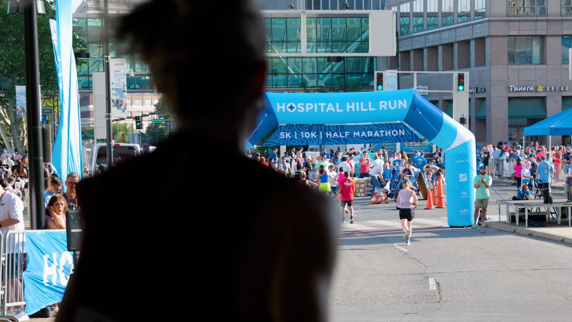 Silhouette of a runner approaching the finish line during the Hospital Hill Run race with spectators looking on.