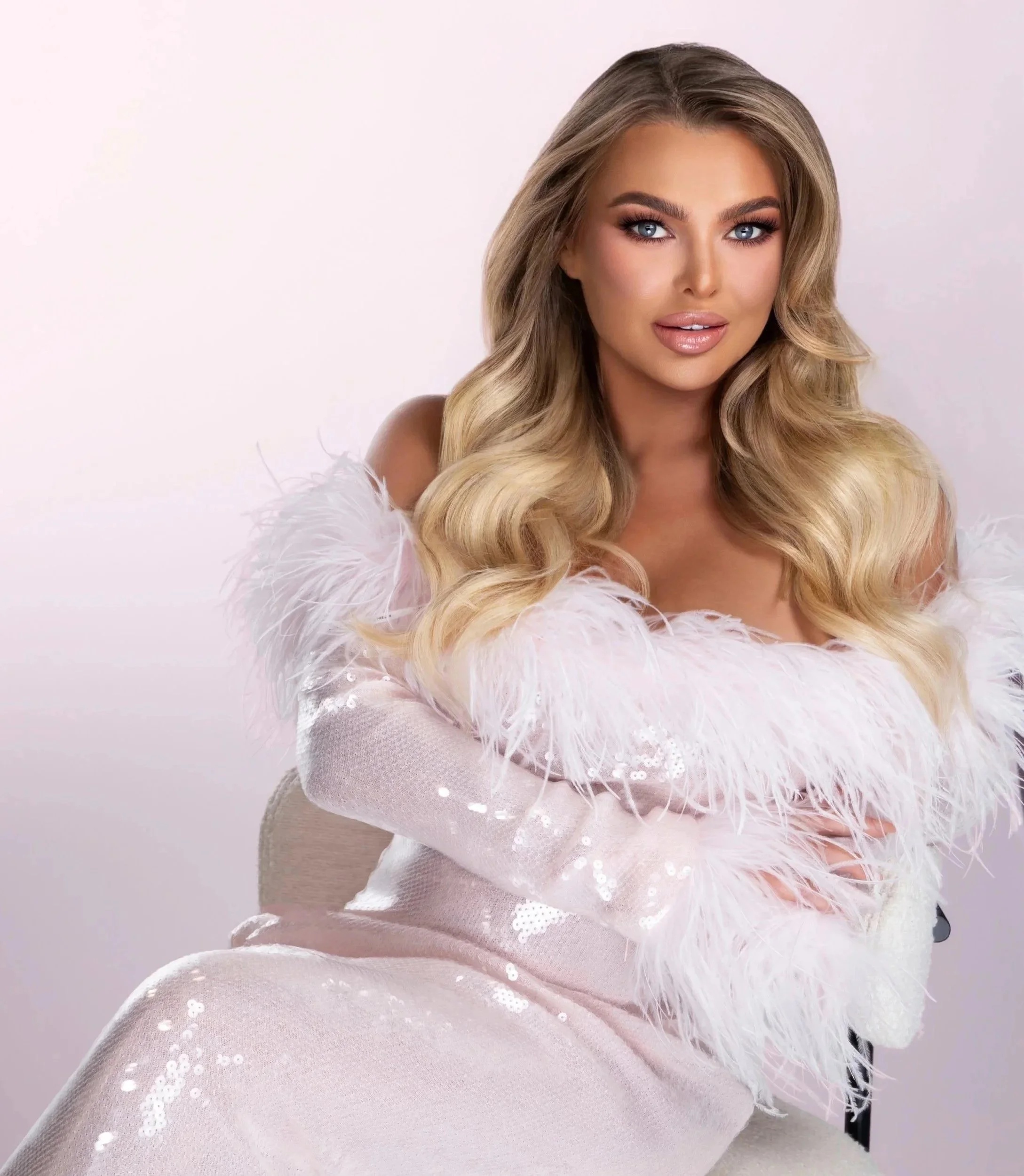 Jessica Robinson -  with long wavy blonde hair and blue eyes wearing a white feathered dress and sheer sleeves.