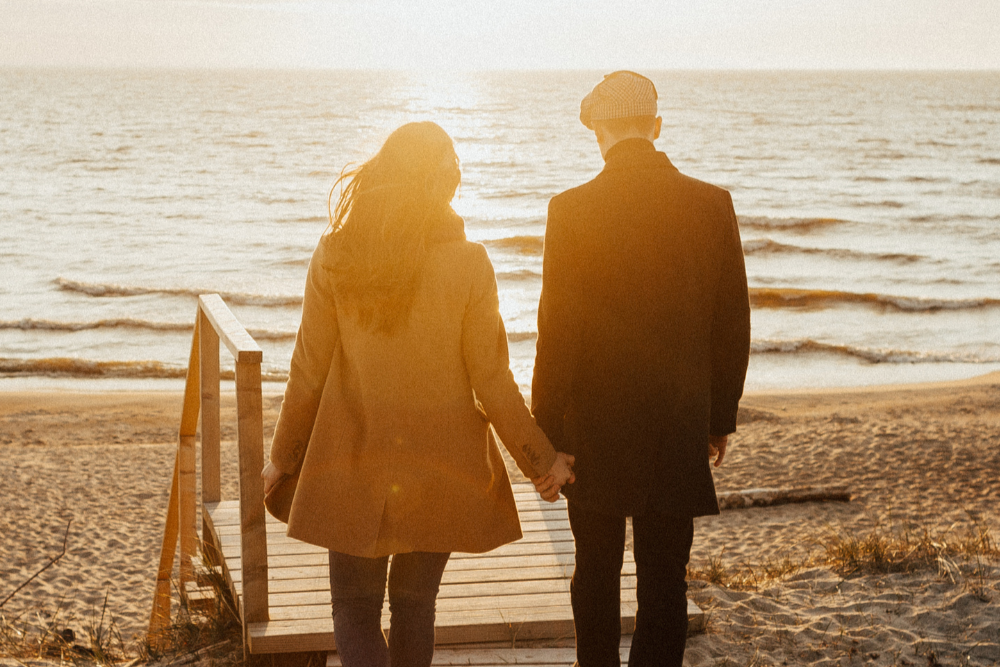 Ein Paar hält sich an einer Strandpromenade am Strand bei Sonnenuntergang. Sie gehen Hand in Hand in Richtung Meer.