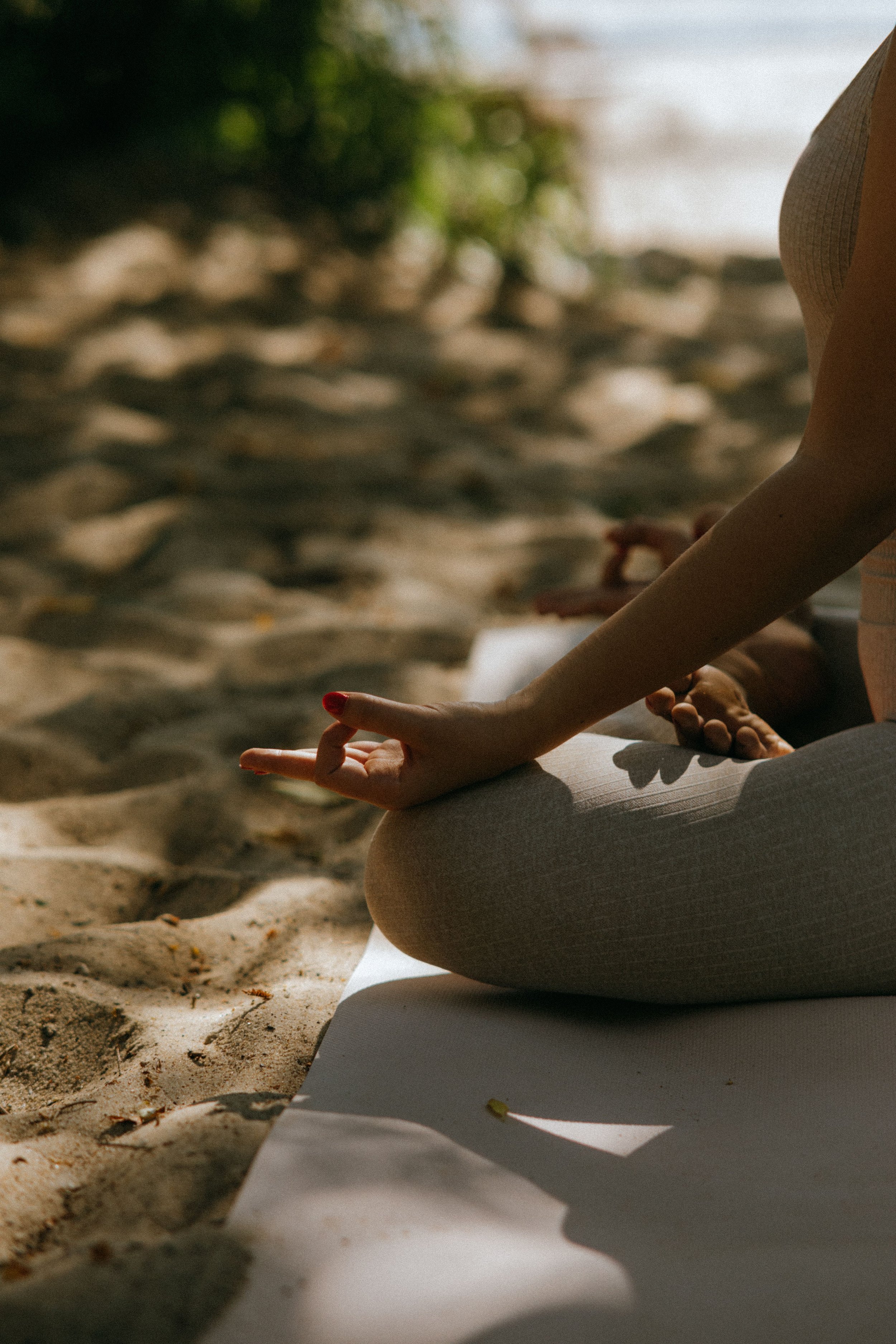 Close-up of a person in a yoga pose on a mat outdoors, with trees and sand in the background.