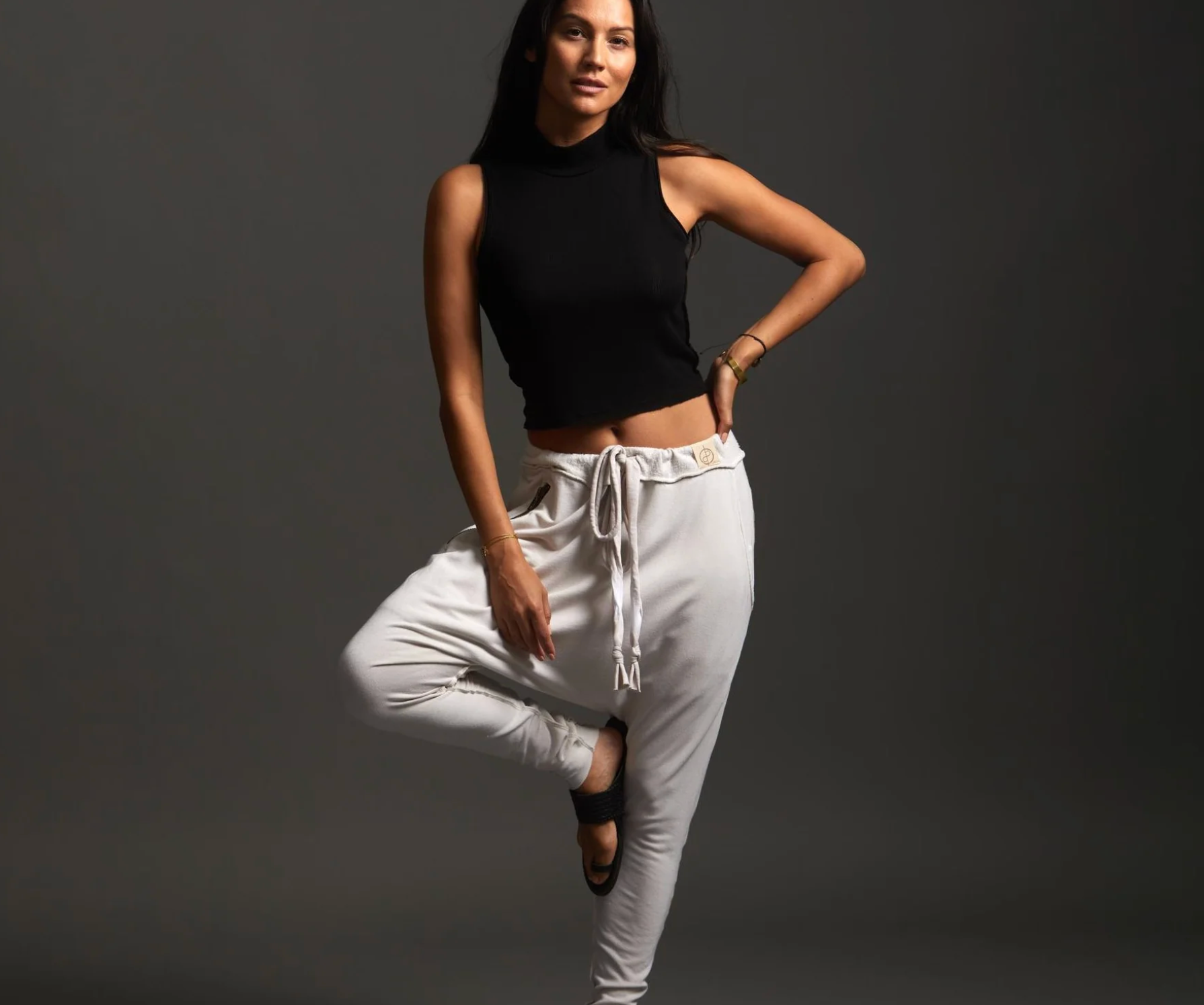 Model wearing One Golden Thread sweatpants and a black top in a yoga-style pose