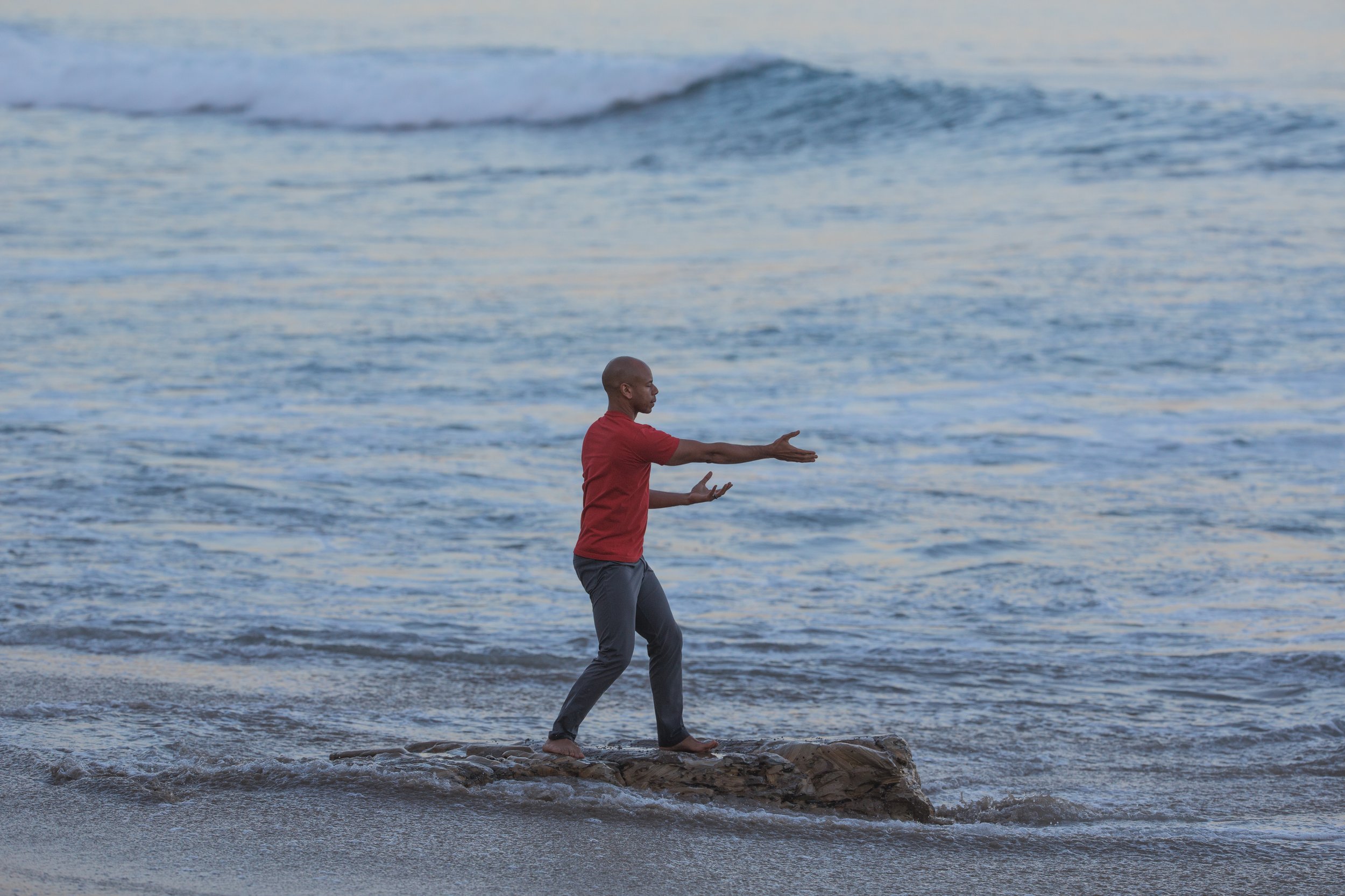 Steven Washington, practicing Qigong barefoot on a rock at the ocean's edge.