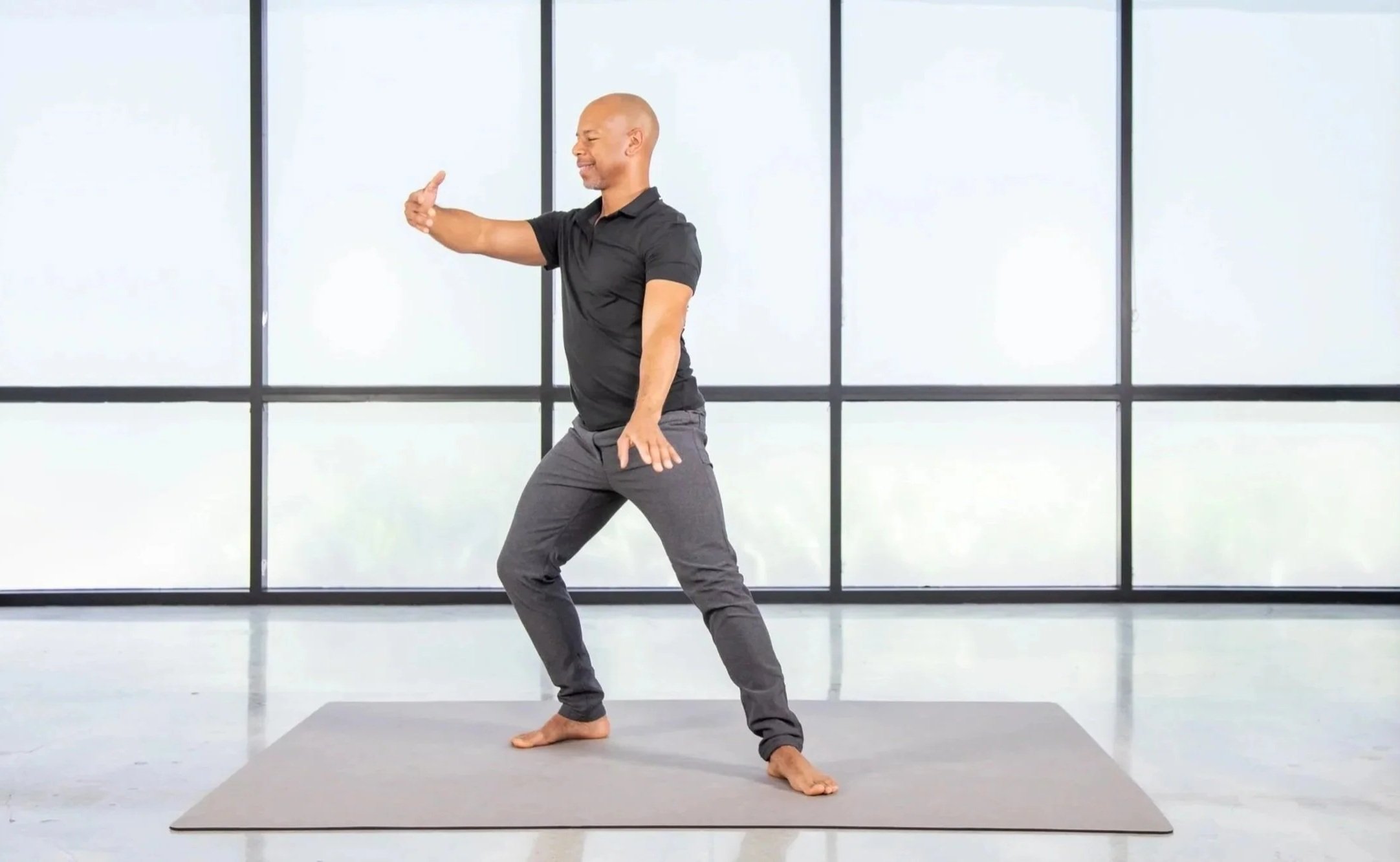 Steven Washington in a wide Qigong stance indoors, in front of large windows.