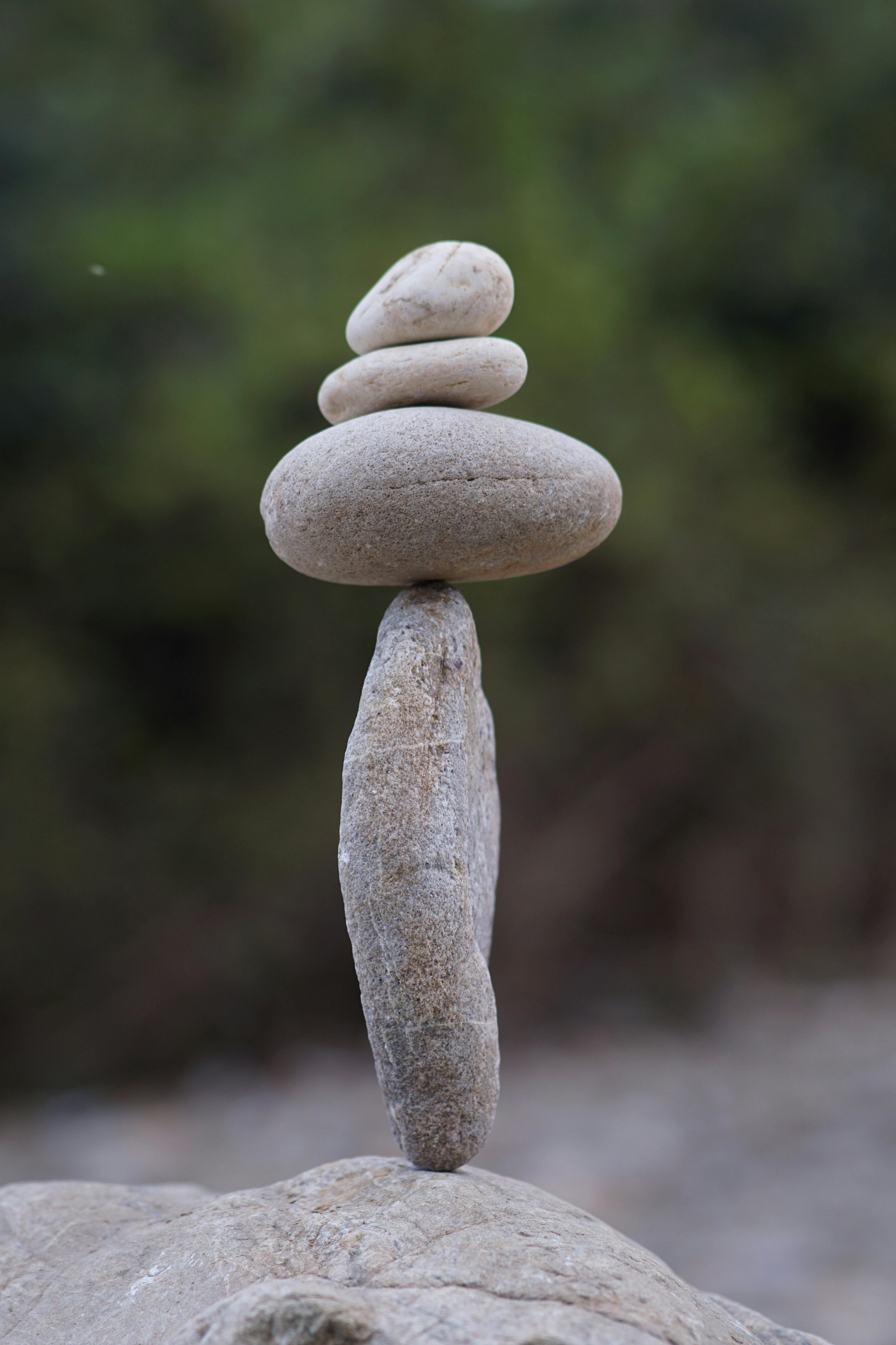 Stacked white and gray stones balanced on a larger stone base against a blurred green background.