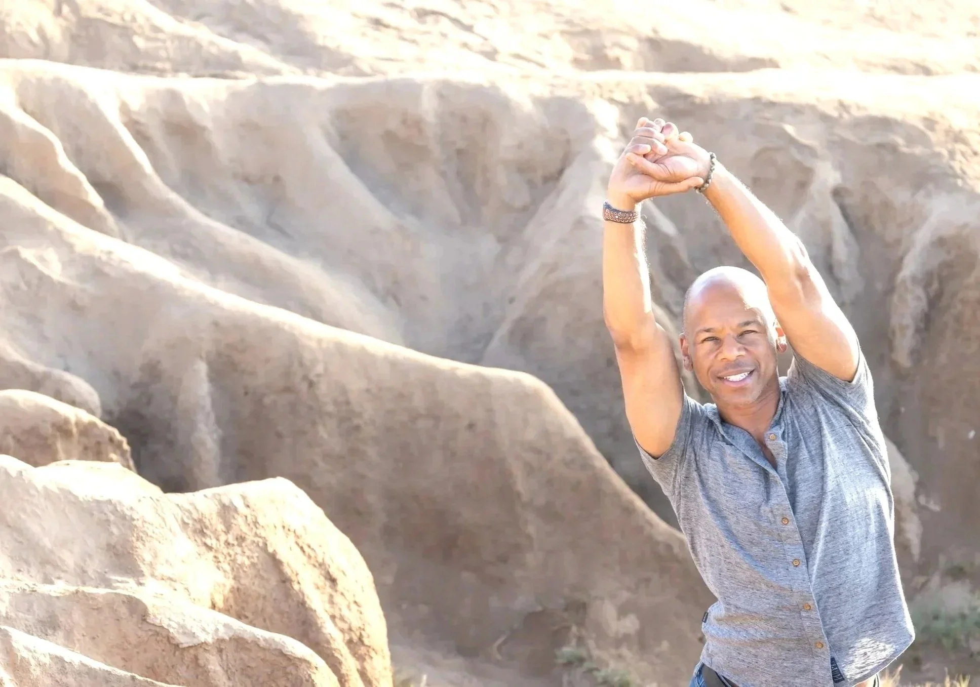 Steven Washington smiling with arms raised overhead, against a rocky desert backdrop