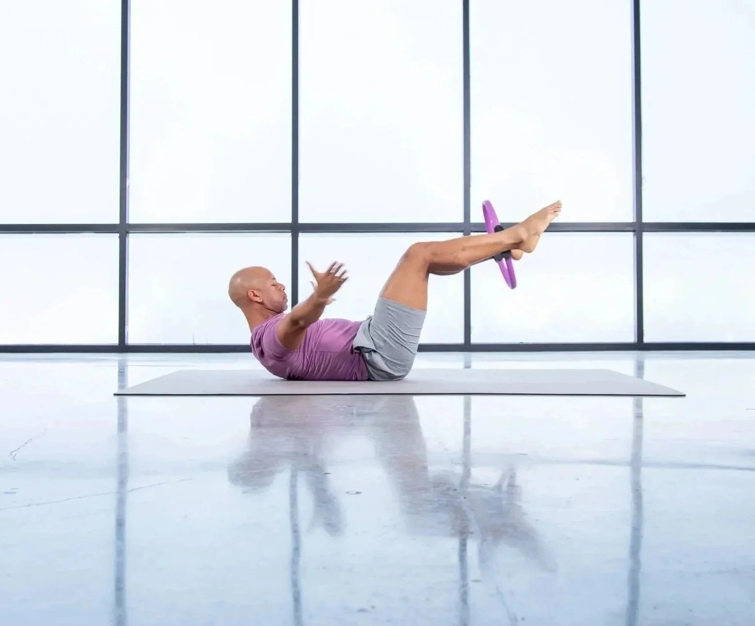Steven Washington performing a Pilates exercise on a mat, using a Pilates ring for resistance.