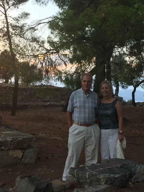 Kostas and Nancy Douzinas standing outdoors near a tree during sunset.