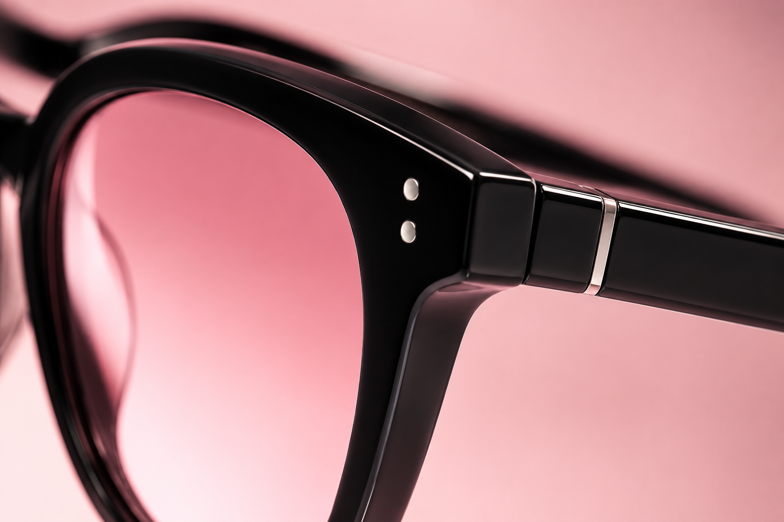 Close-up of black eyeglass frame with silver detailing on a pink background.