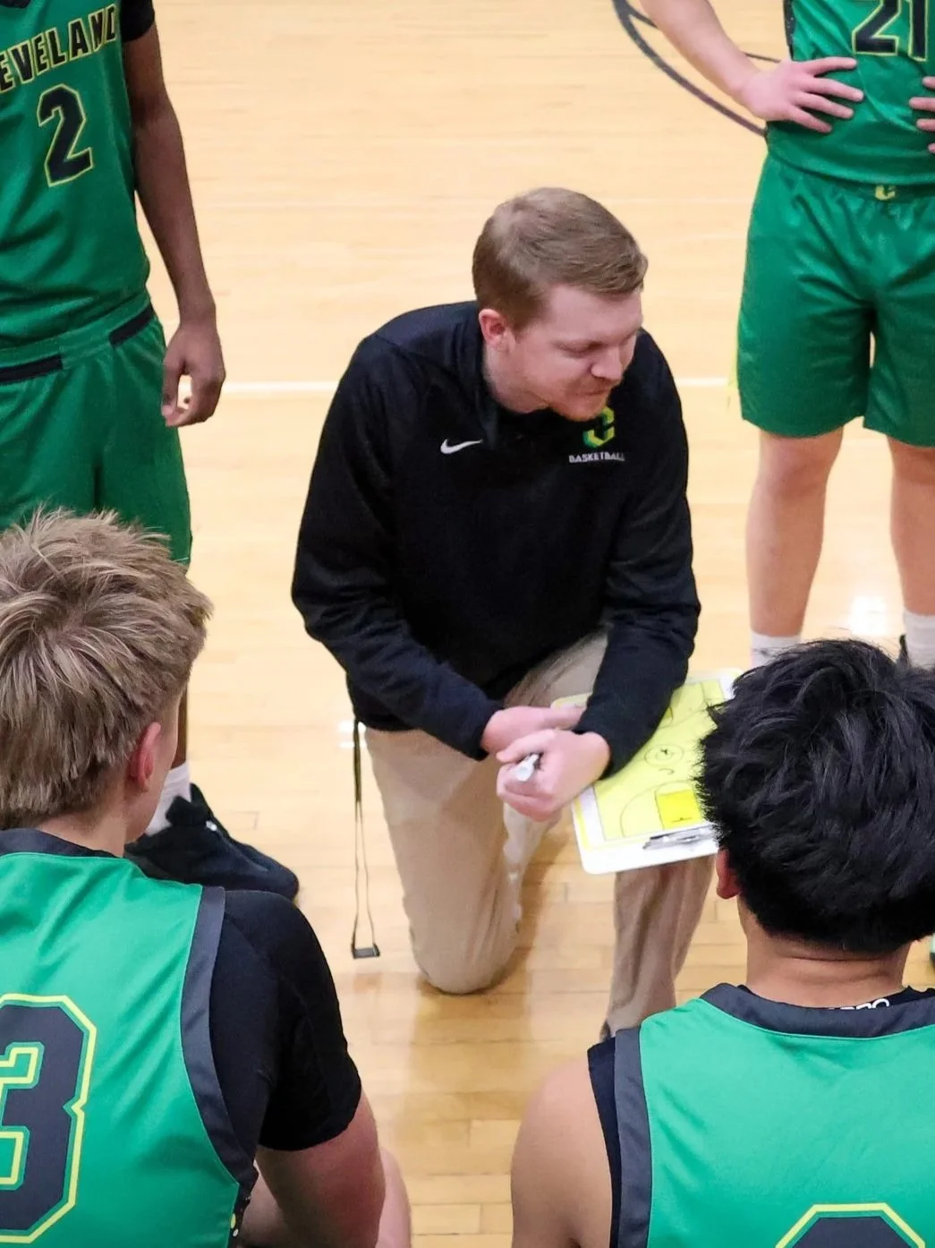 Basketball coach kneeling with players during a timeout on the basketball court.