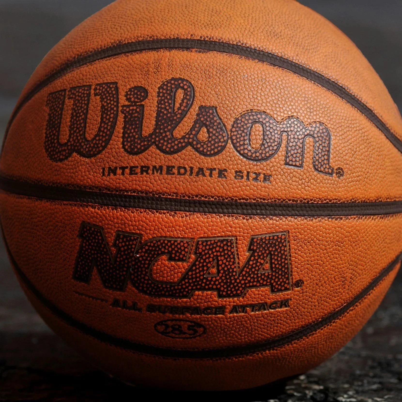 A Wilson basketball on a dark surface, showing an orange textured surface with black lettering and details.