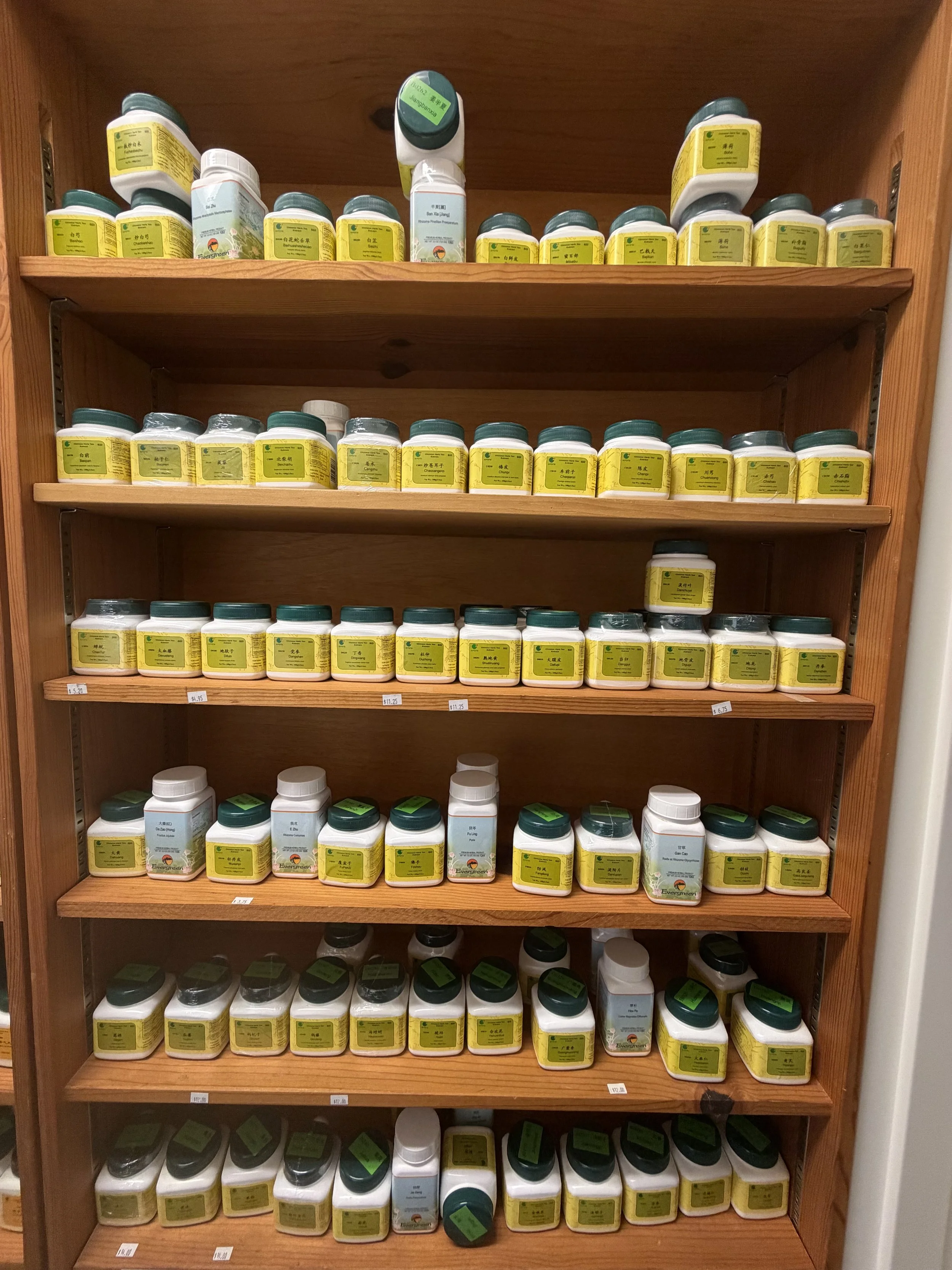 A wooden shelf stocked with numerous bottles of traditional Chinese medicinal herbs, labeled in Chinese characters.