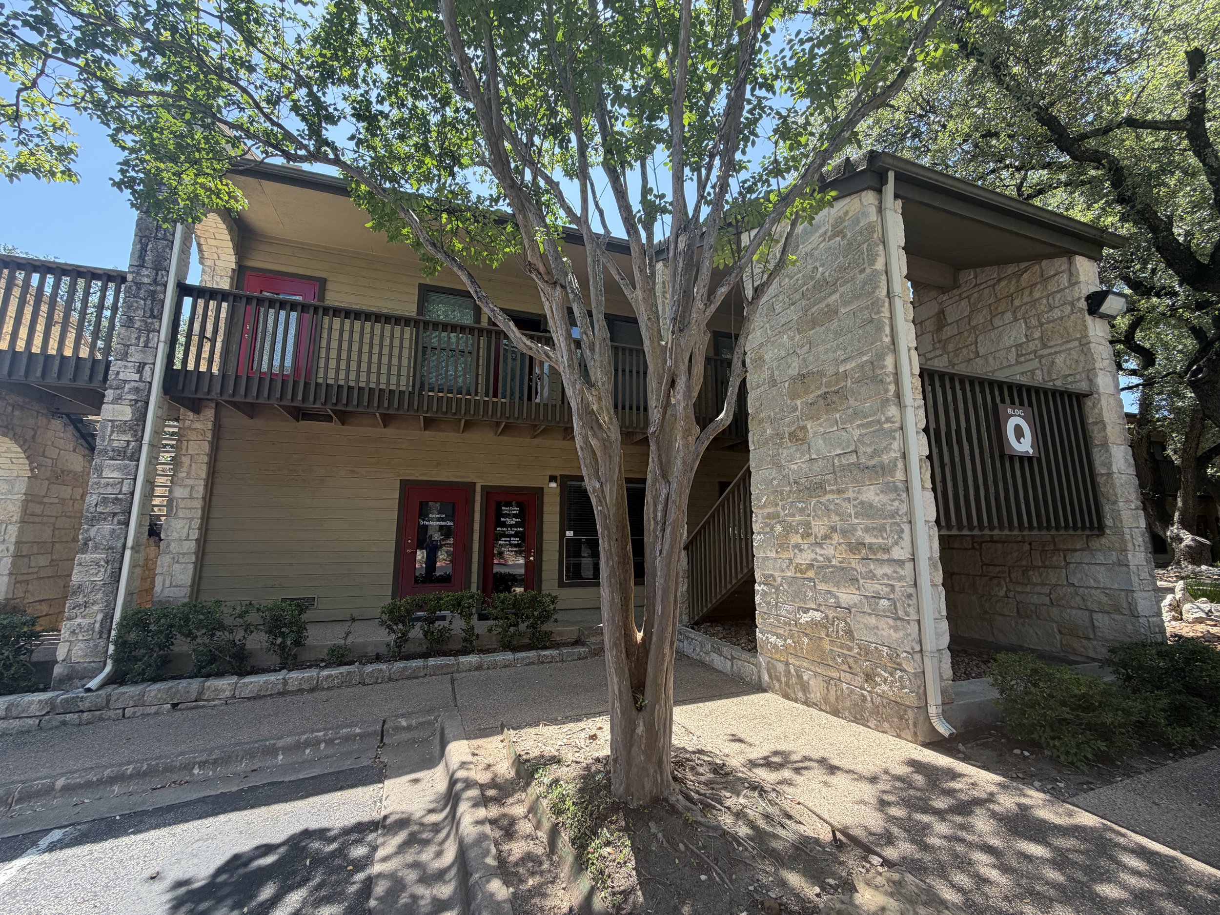 A two-story building with stone and wood exterior, trees in front, and a sidewalk.