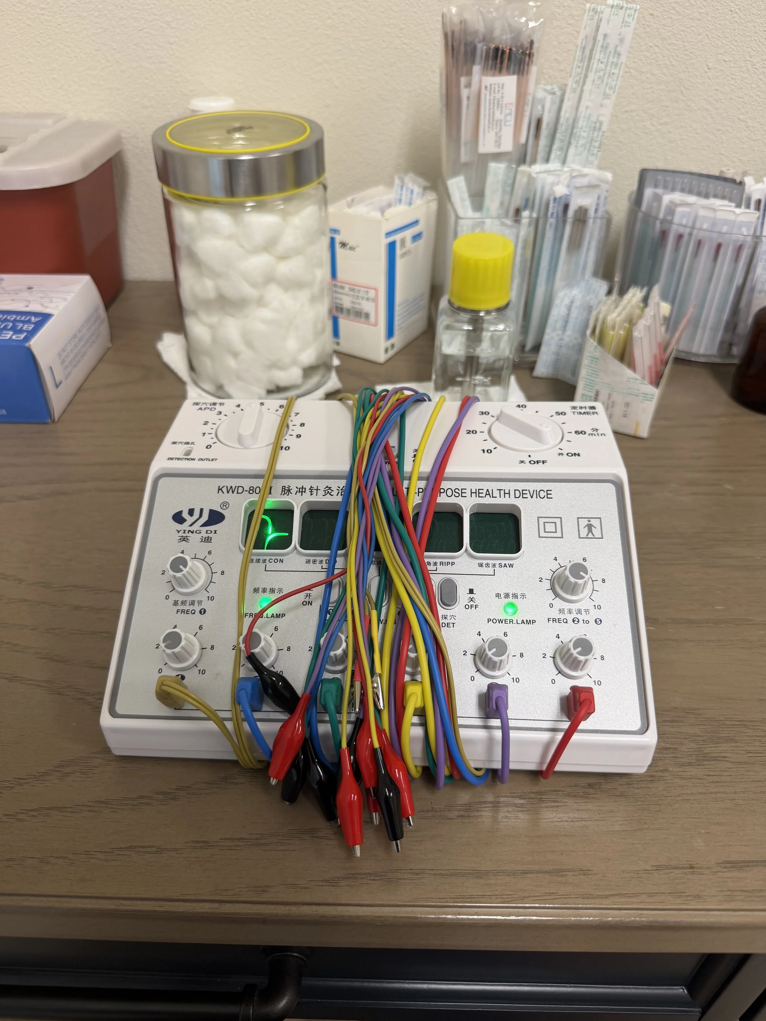A medical device with colorful wires connected to it, placed on a wooden table with medical supplies in the background.