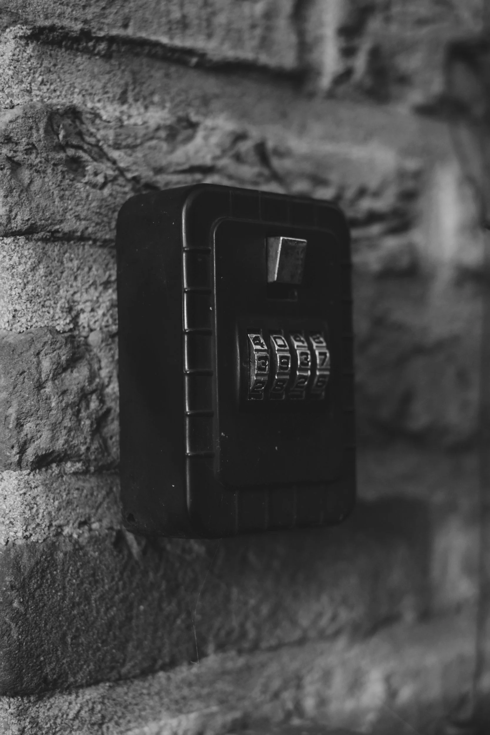 A close-up black-and-white photograph of a combination lock attached to a textured rough stone wall.