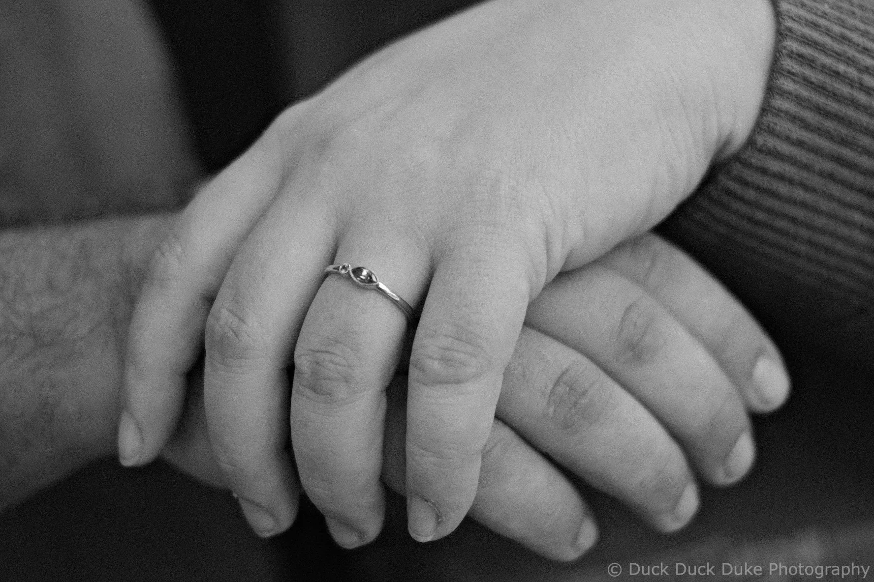 Close-up of a person's hand with a ring on the ring finger, in black and white.