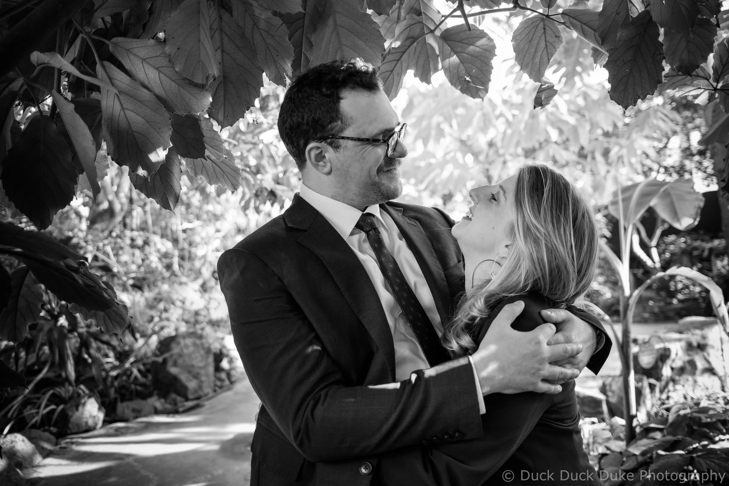 Man and woman embracing outdoors with trees and foliage in the background