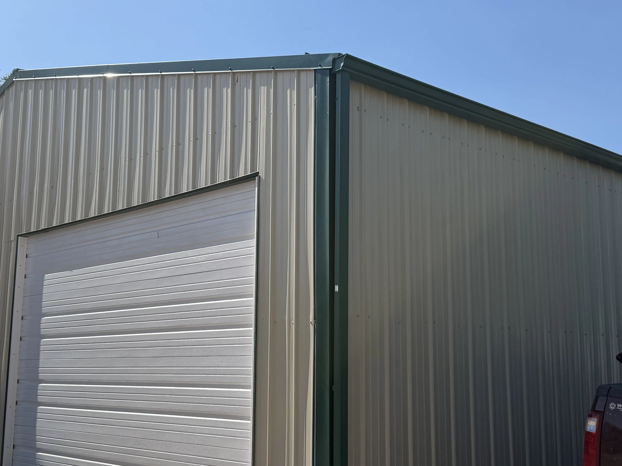 The photo shows the exterior of a building with metal siding and a partially open white garage door, against a clear blue sky.