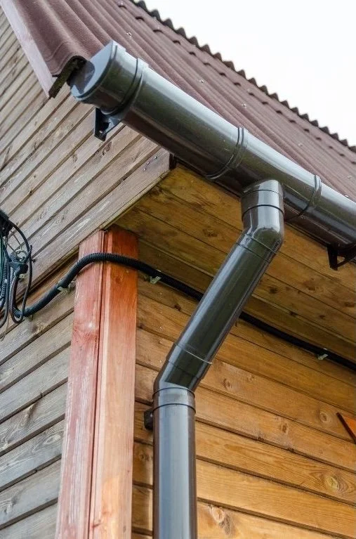 Black rain gutter system attached to the corner of a wooden house exterior.