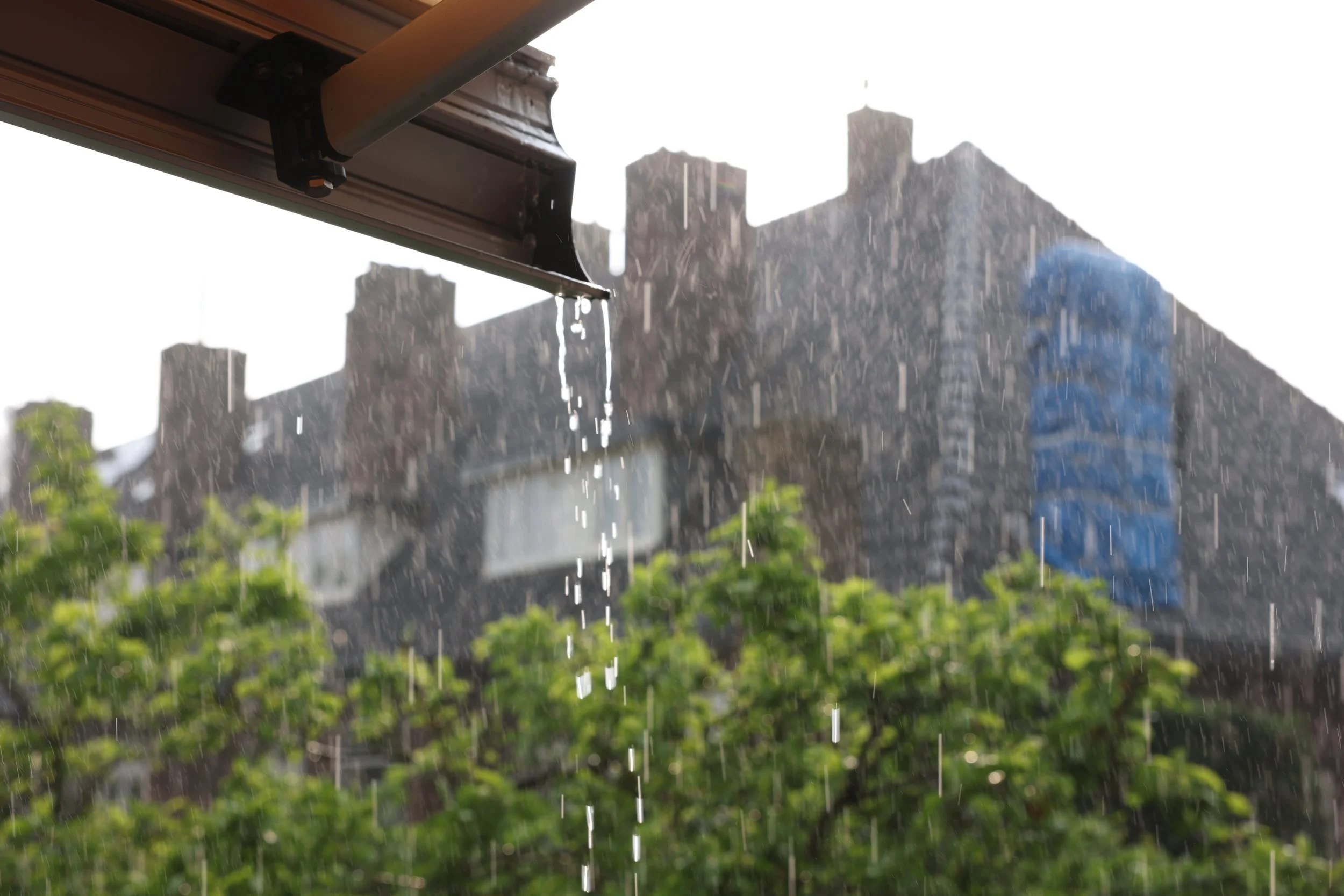 Rain falling from an overhang with city buildings in the background.