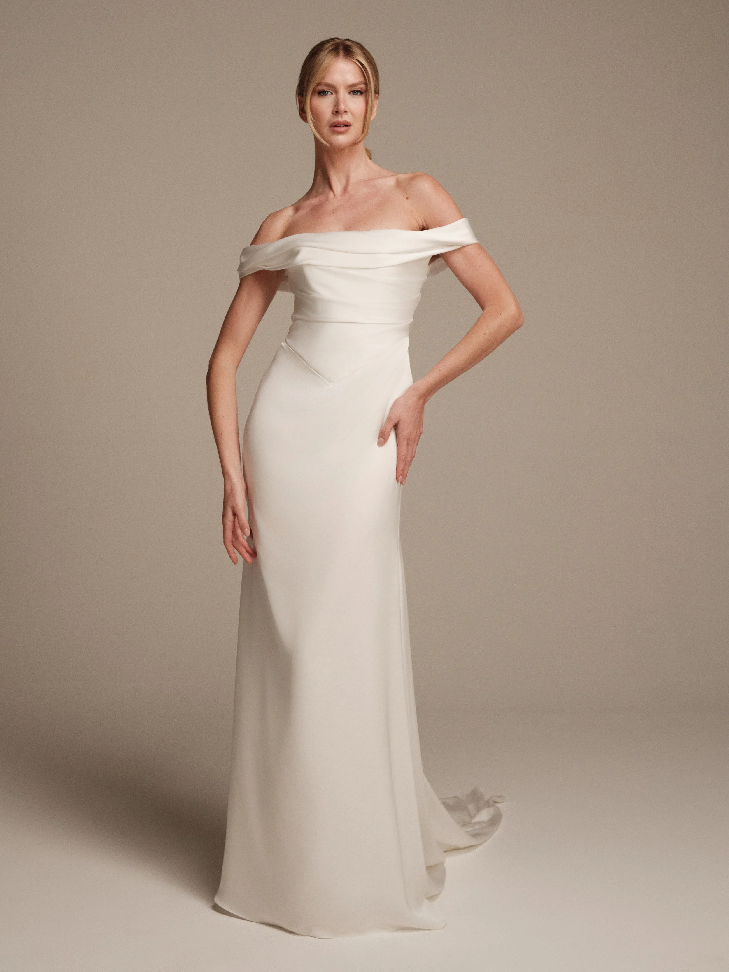 Discover Eos by Maria Pia, a liquid satin wedding dress with a sculpted off-the-shoulder neckline, softly draped bodice, fitted silhouette and sweeping train.