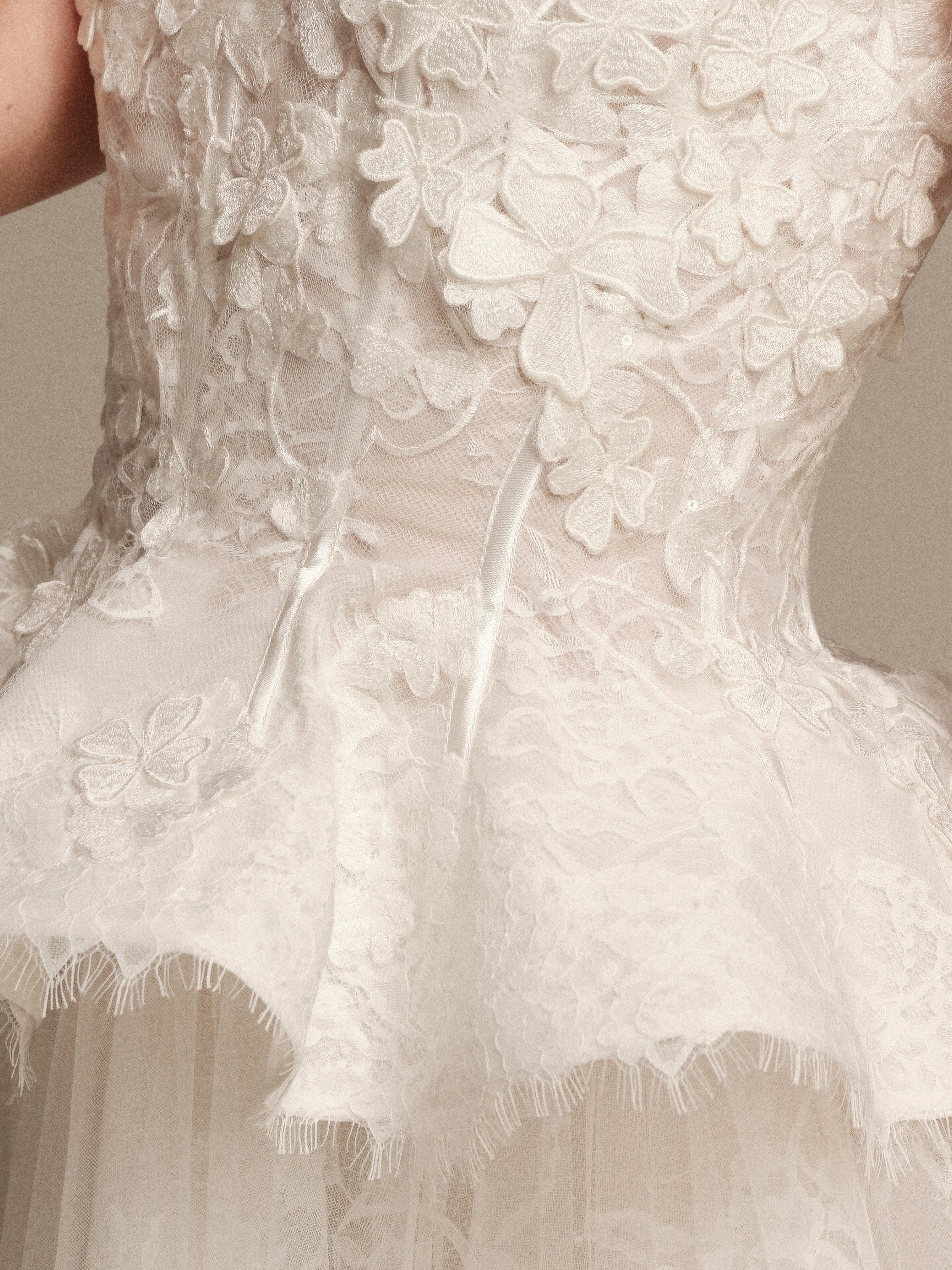 Close-up of Gaia strapless bridal gown with dimensional 3D floral lace petals and peplum waist