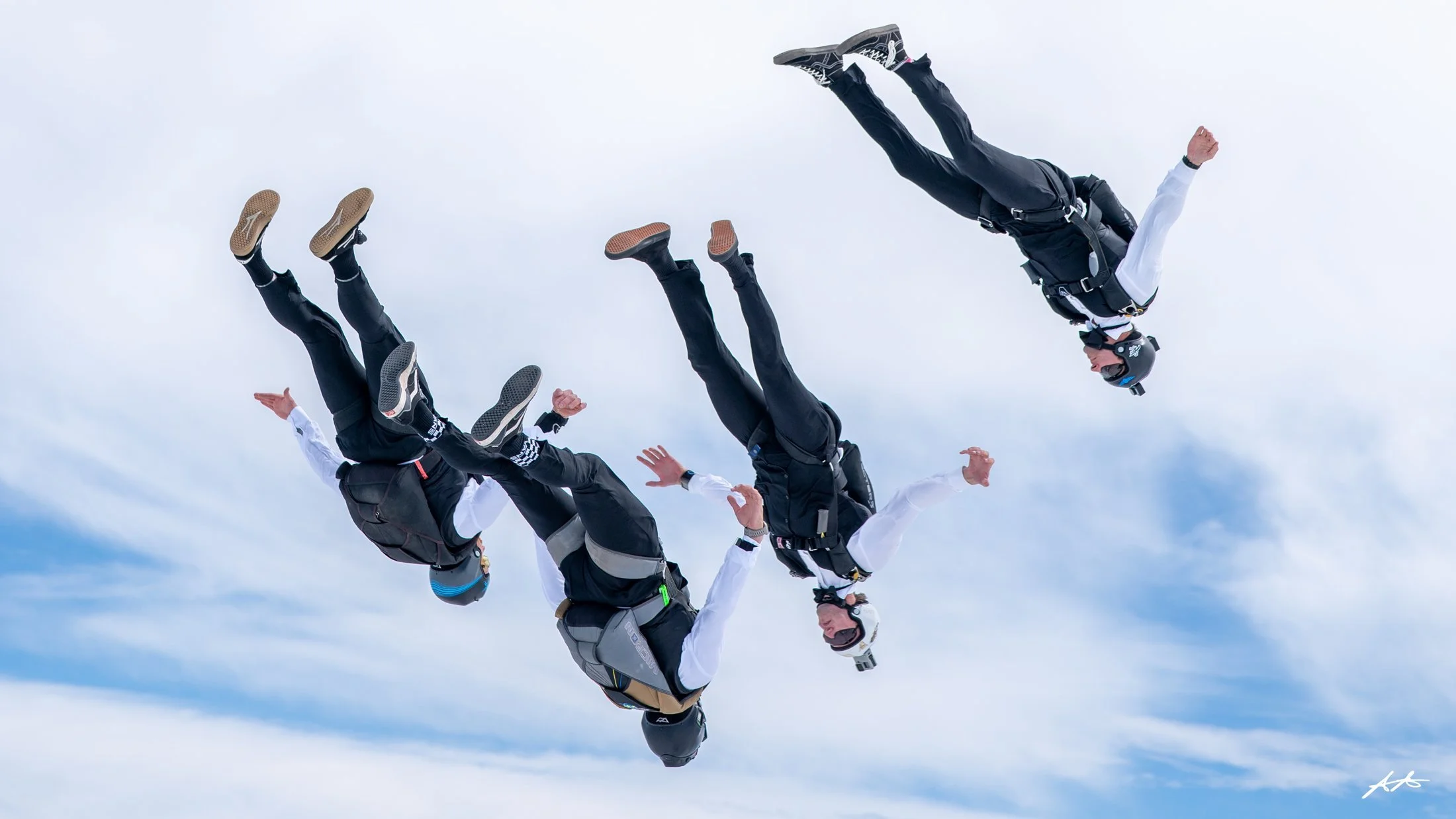 A group of skydivers falling through the sky with clouds in the background.