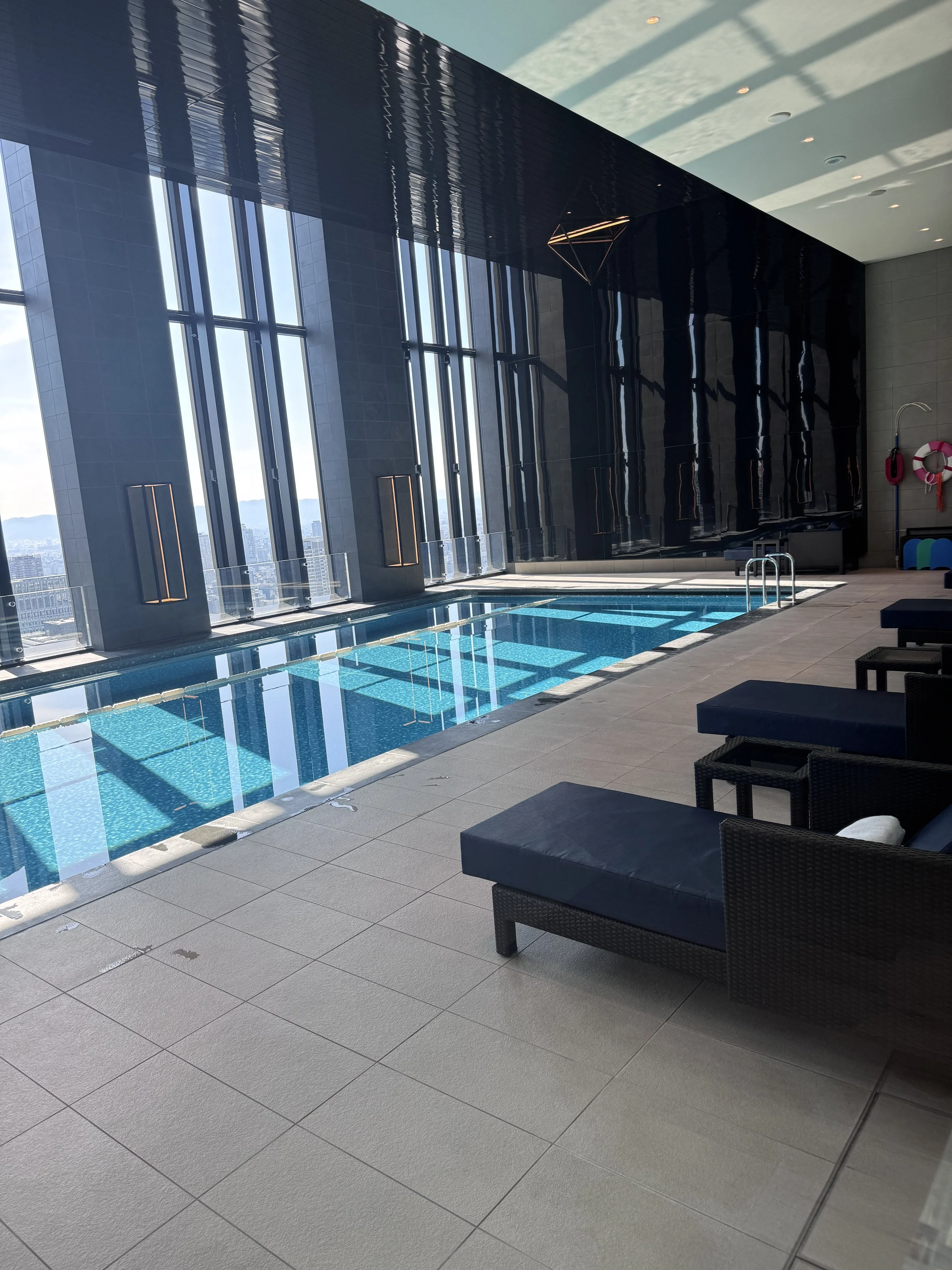 Indoor pool at Conrad Osaka with skyline windows and lounge chairs