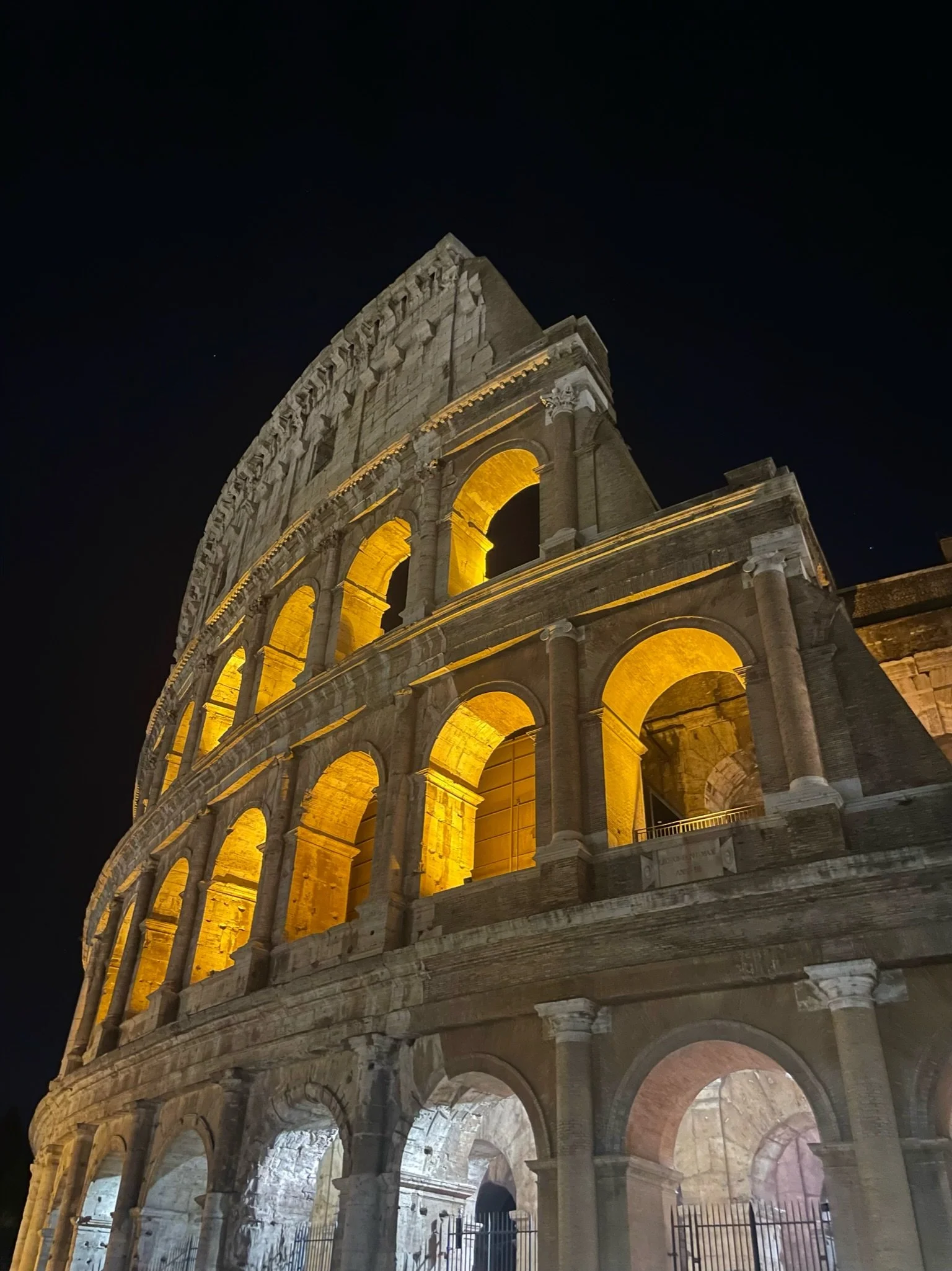 Night view of the illuminated Colosseum in Rome, Italy, showcasing its arches and ancient architecture against a dark sky.