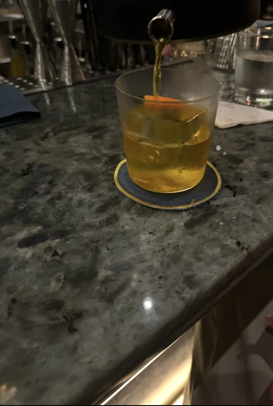 Bartender pouring a cocktail over a large ice cube at Bar Trigona