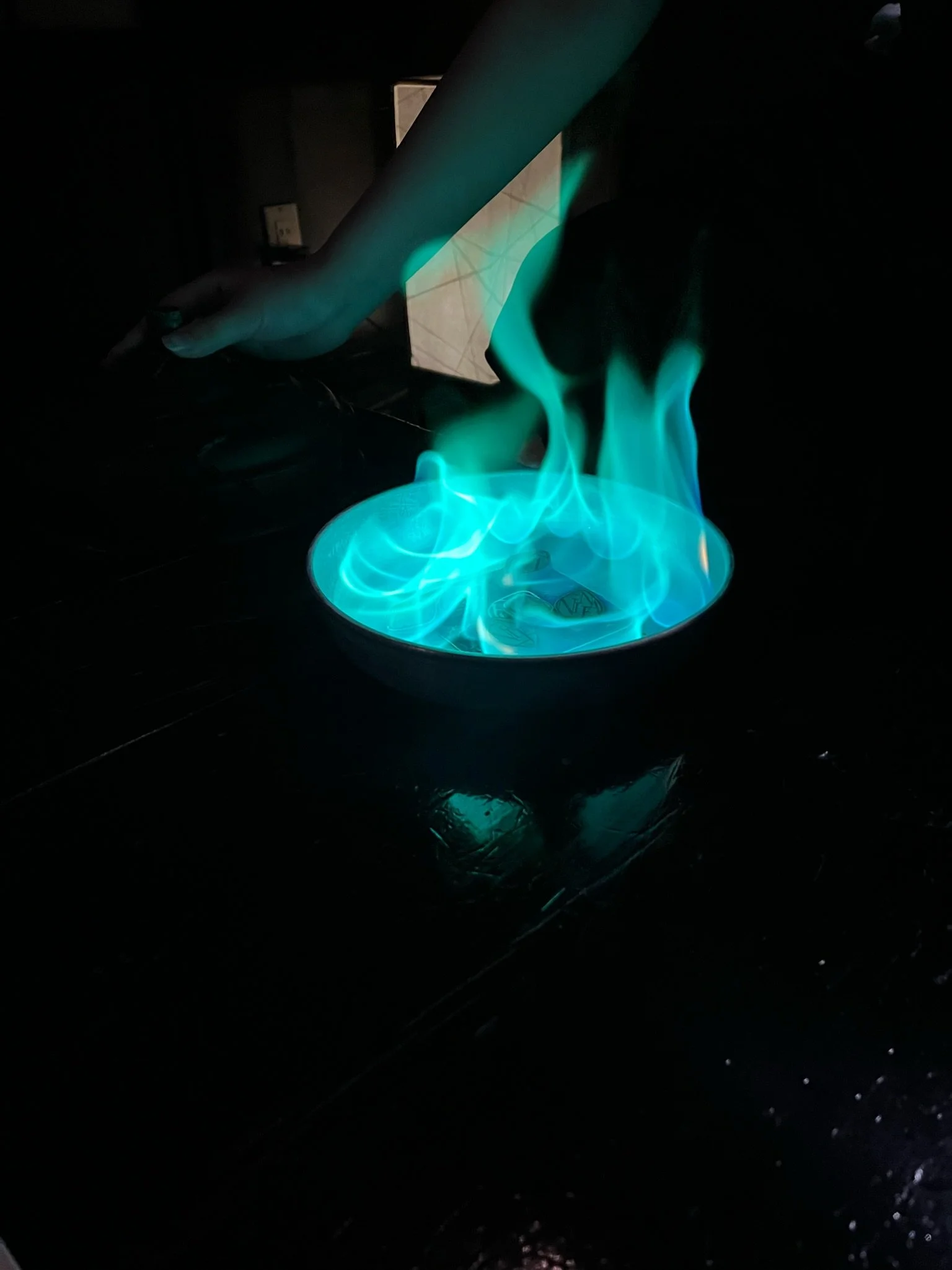 A hand using tongs to handle a piece of dry ice, with blue flames and vapor emanating from the dry ice, in a dark setting.