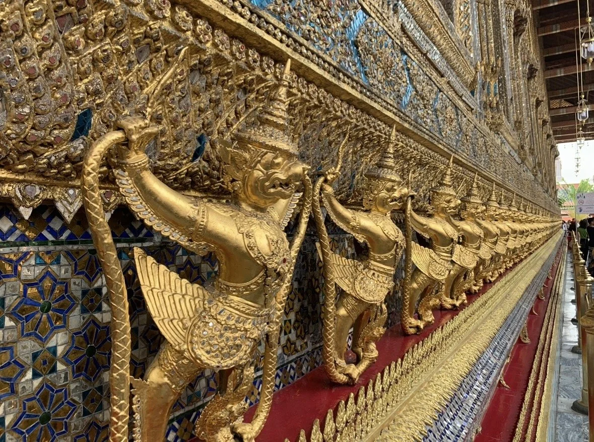 A row of intricately detailed golden demon statues holding spears, lining a decorated wall in a temple.